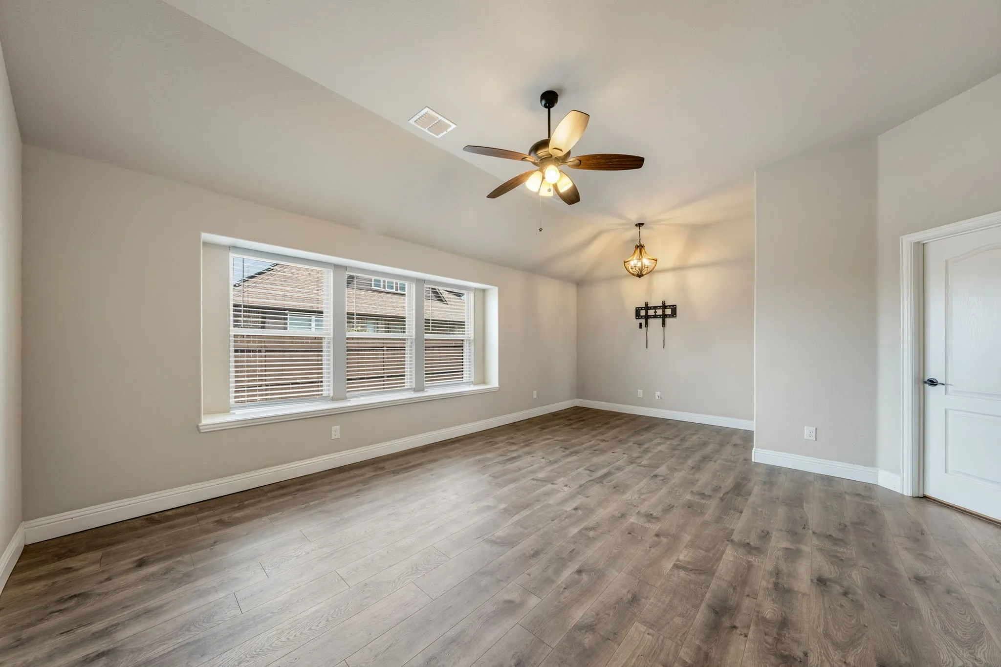 Spacious room featuring wood-finish flooring, a multi-pane window with blinds, a ceiling fan, and a chandelier