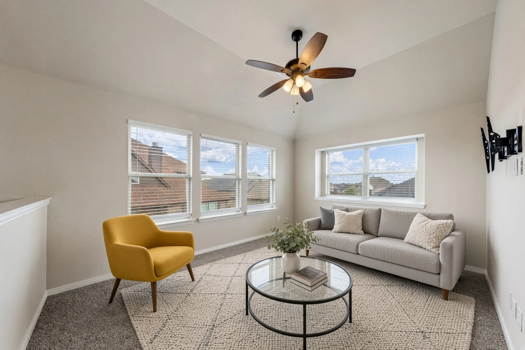 Vaulted ceiling with a ceiling fan, multiple windows with blinds, wall-mounted television bracket, and carpeted flooring
