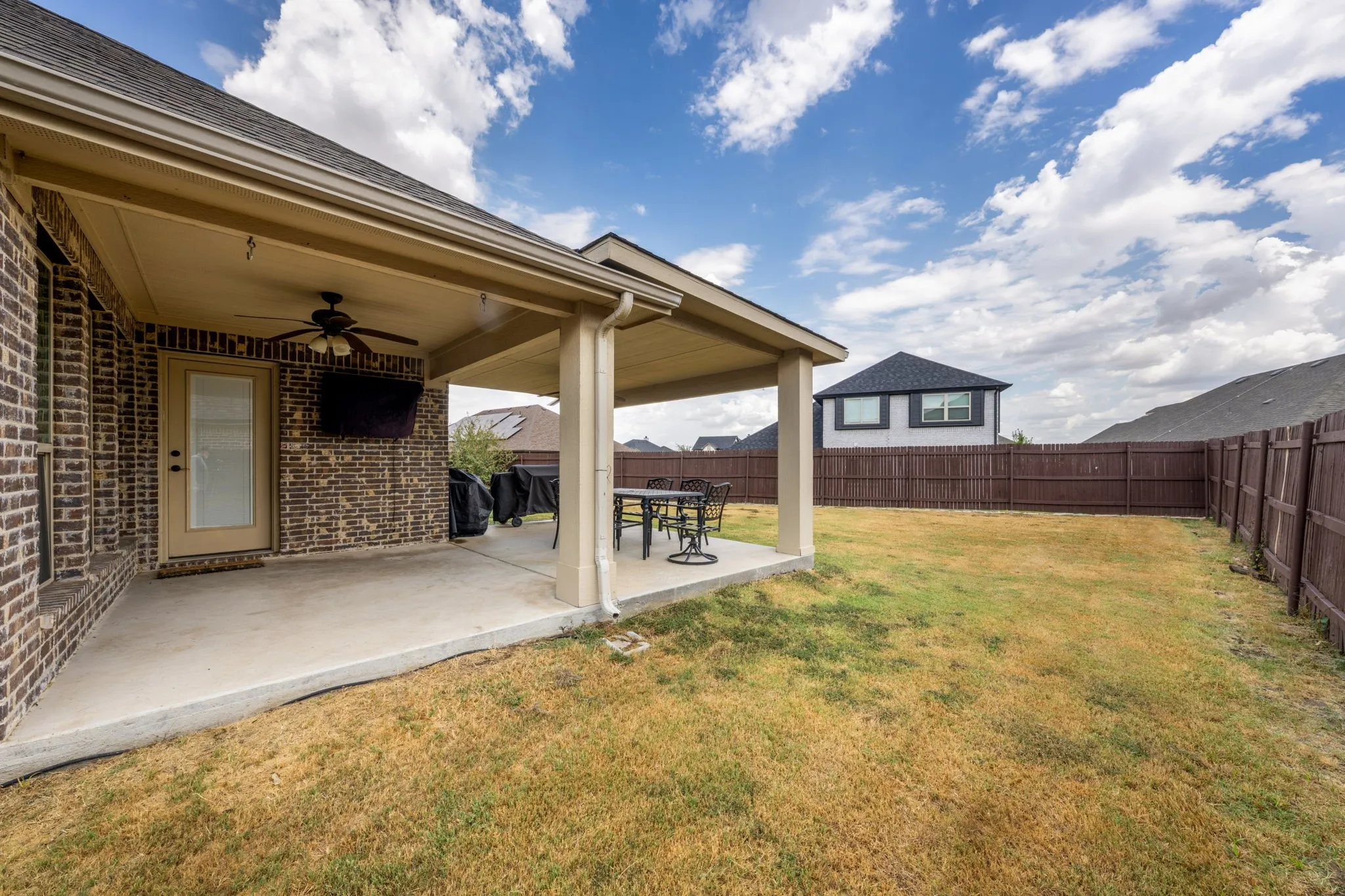 Covered patio with a ceiling fan, brick exterior, concrete flooring, and an expansive fenced backyard