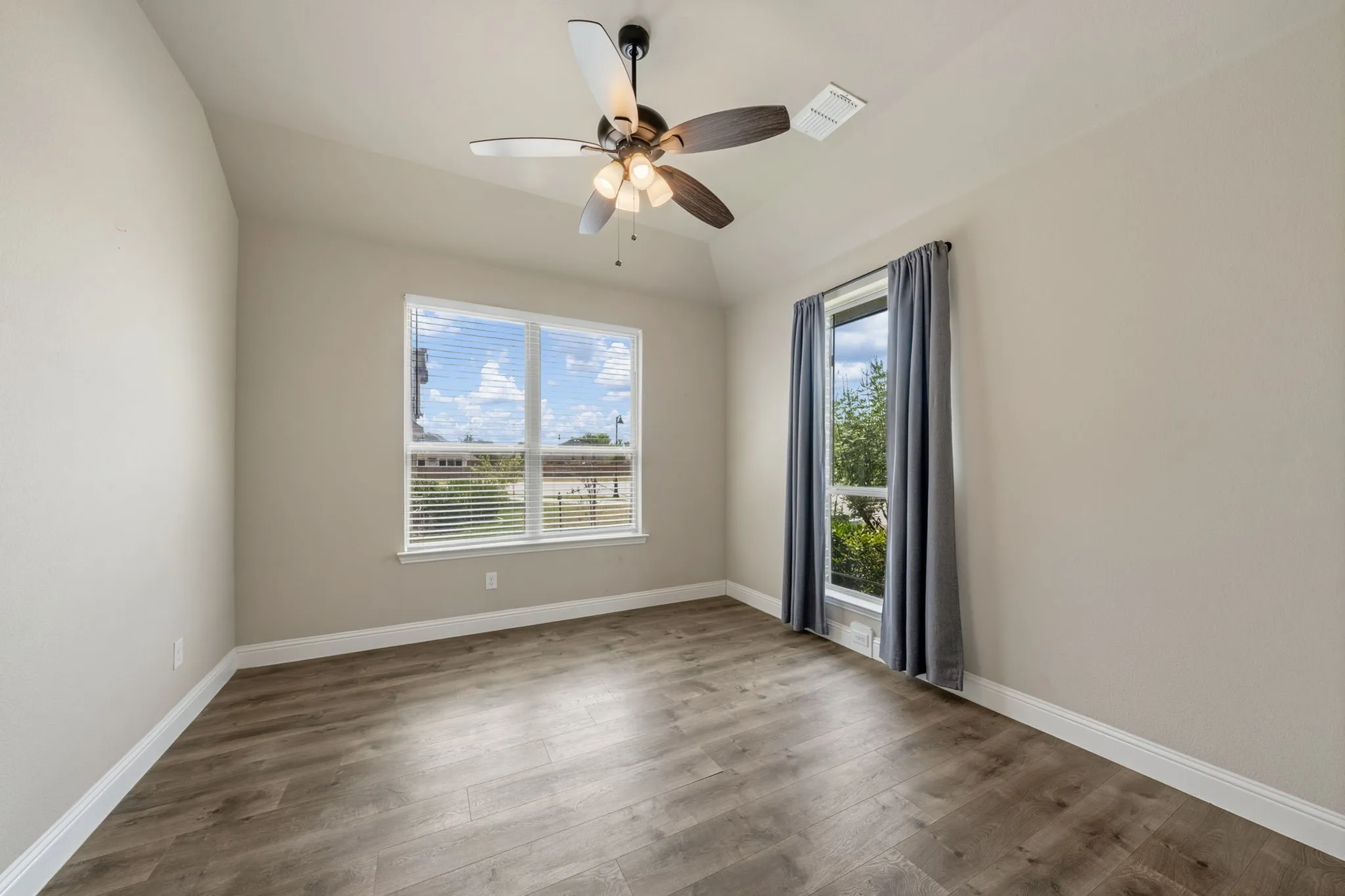 Wood-finish flooring, vaulted ceiling, ceiling fan with integrated lighting, and two windows providing natural illumination