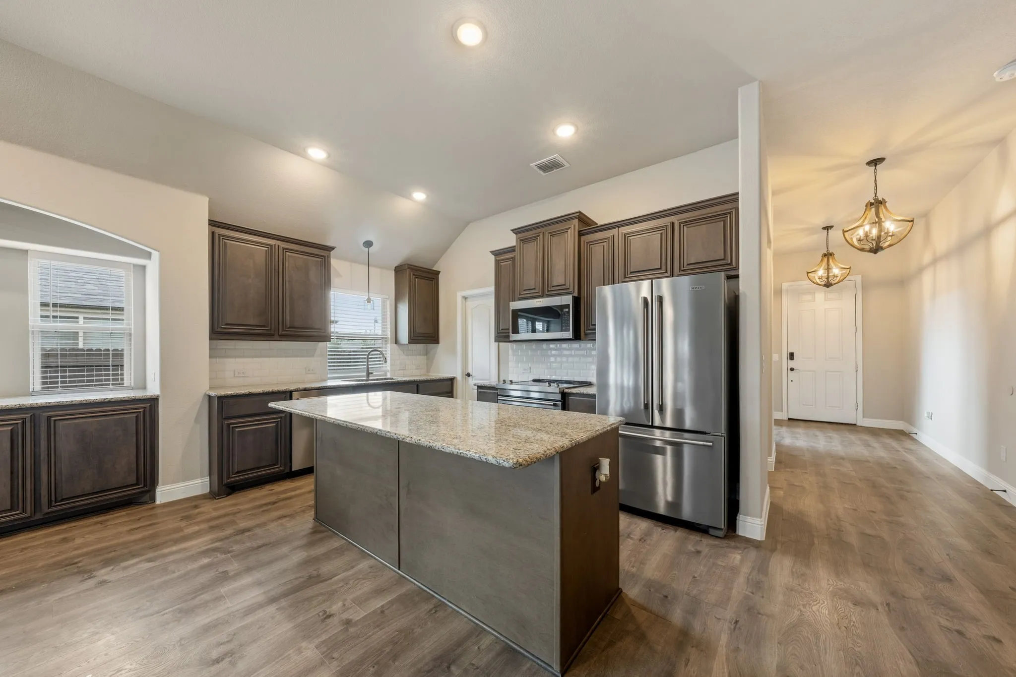 Kitchen featuring an island with granite countertop, wood-finish flooring, stainless steel appliances, dark wood cabinetry, and recessed lighting