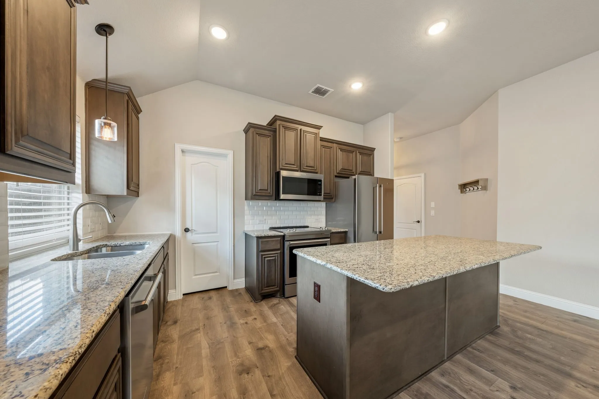 Kitchen featuring wood-finish flooring, recessed lighting, a central island with a granite countertop, stainless steel appliances, and wood cabinetry