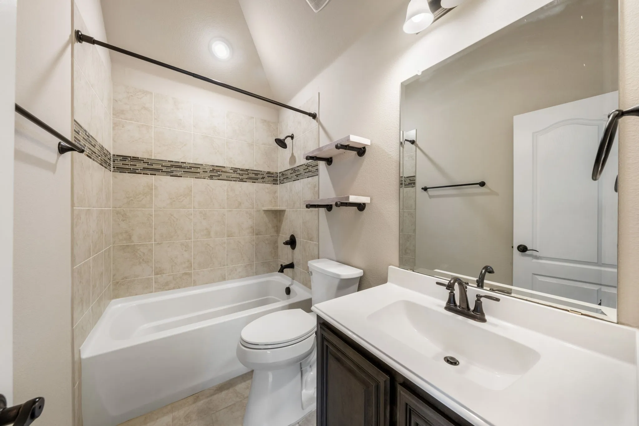 Tile shower surround with mosaic accent, built-in bathtub, vanity with integrated sink, dark wood-finish cabinetry, and wall-mounted mirror