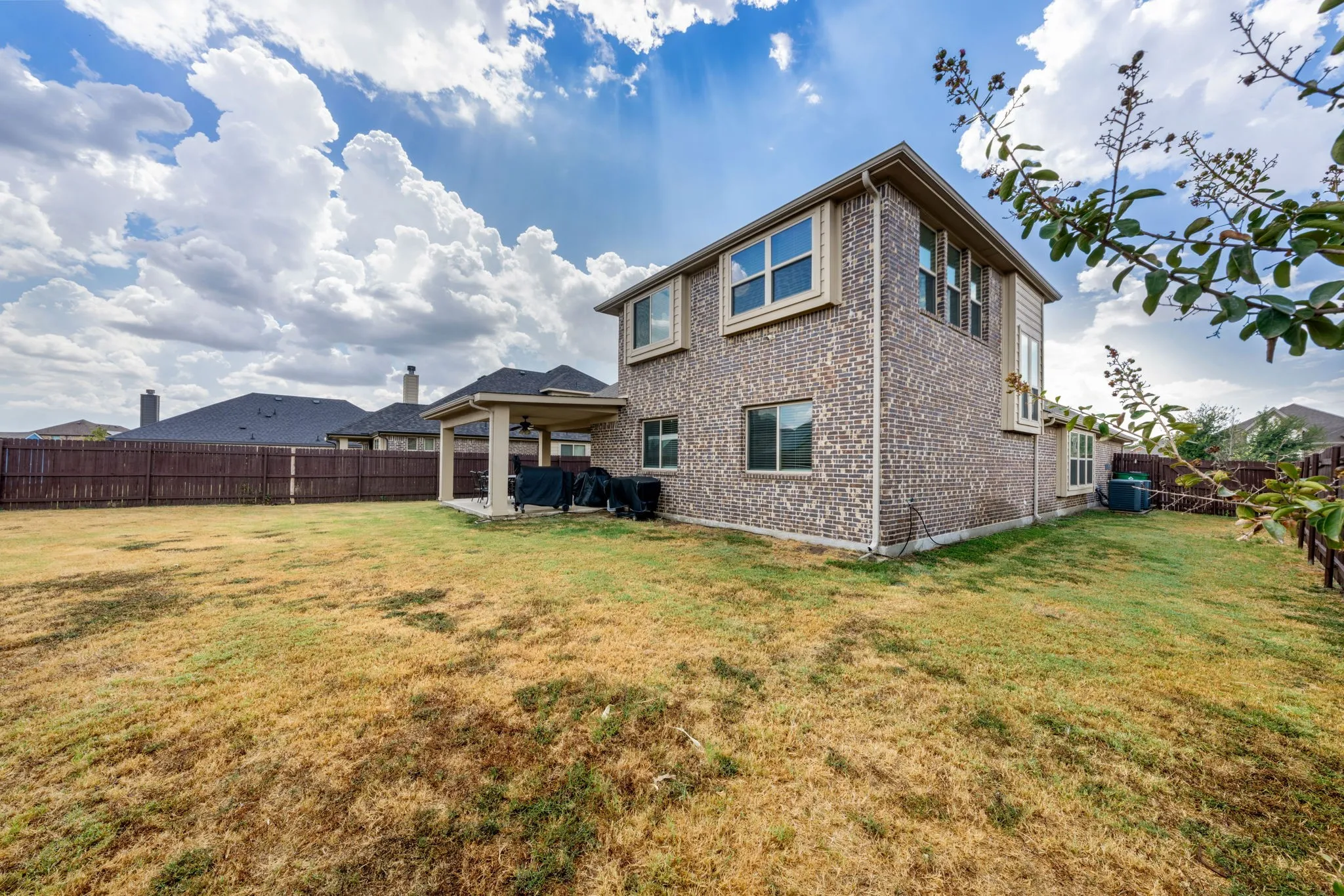 Expansive backyard featuring a covered patio, brick exterior, multiple windows, and a wood privacy fence