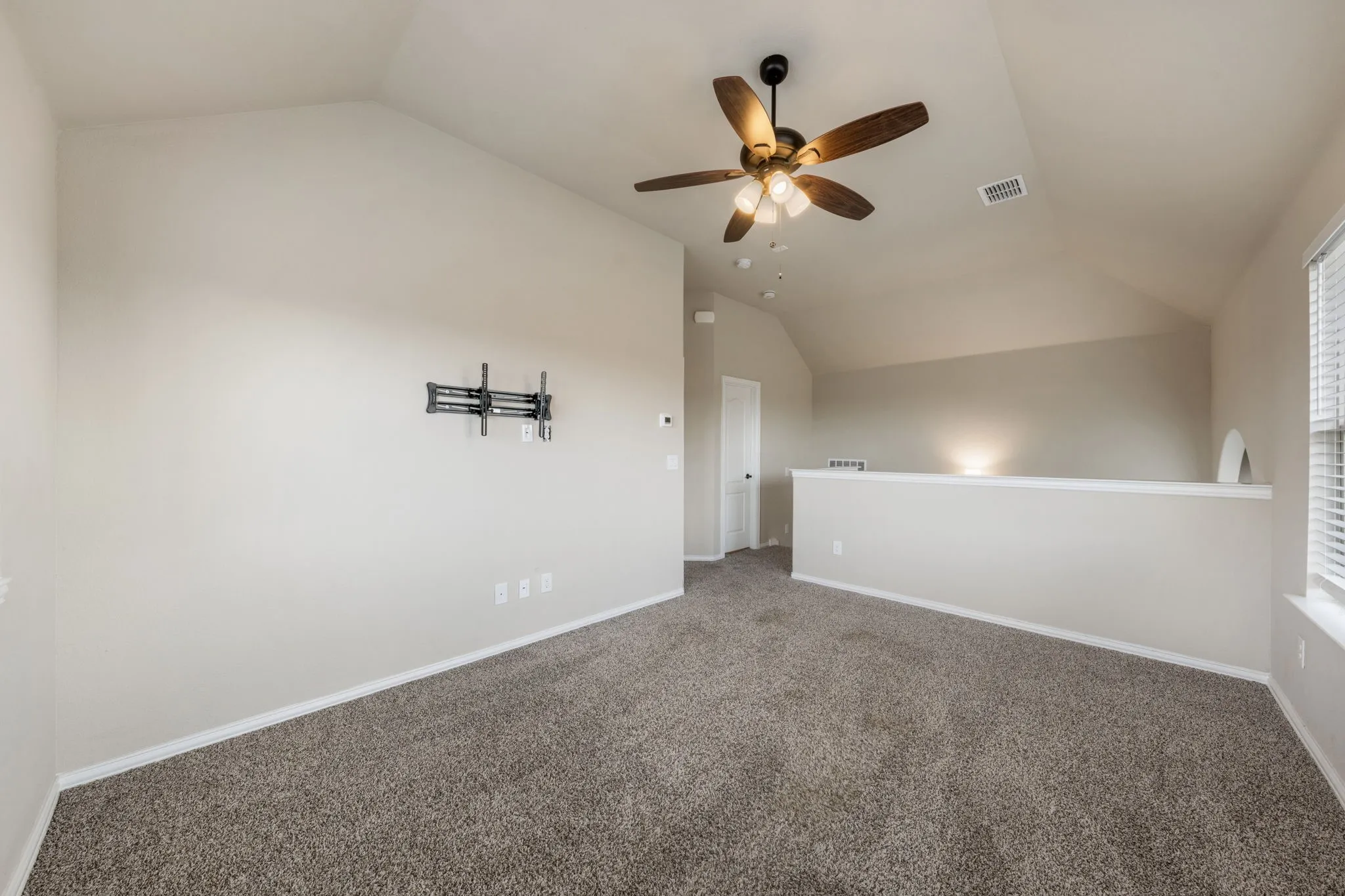 Carpeted room with a vaulted ceiling, a ceiling fan with light fixture, and a built-in wall partition