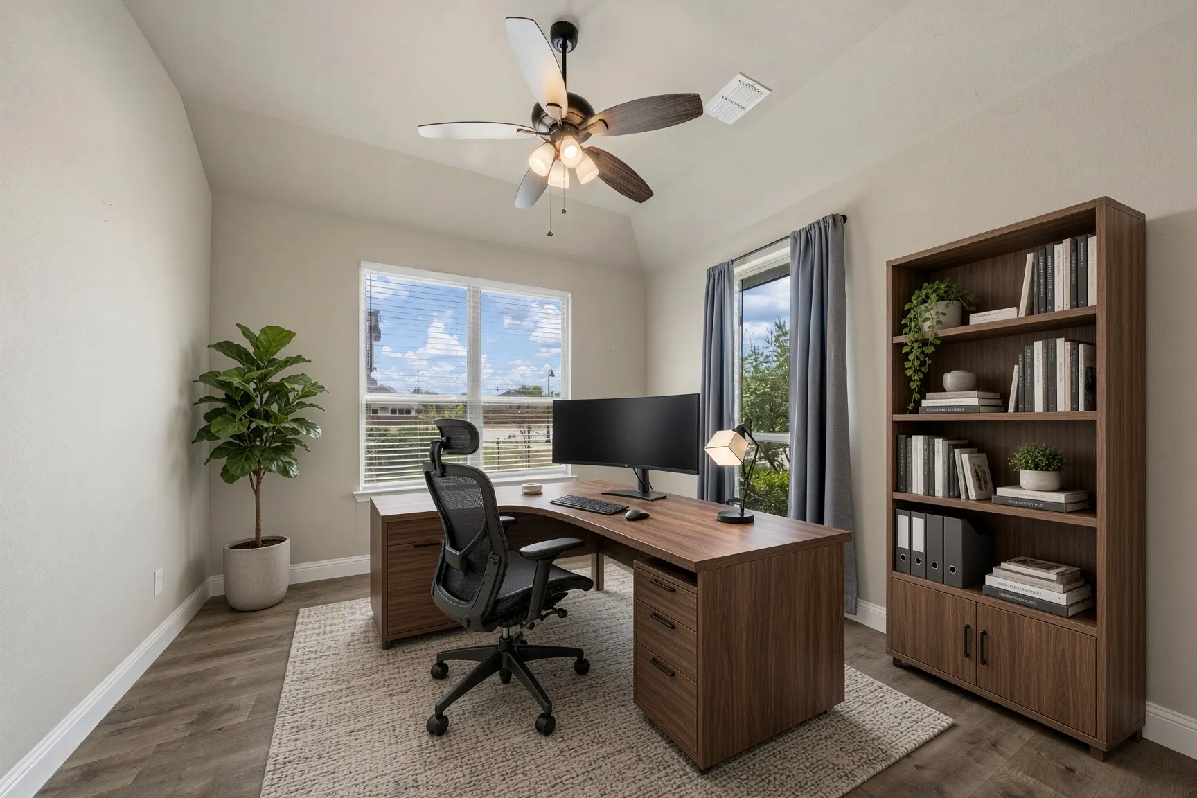 Vaulted ceiling, wood-finish flooring, ceiling fan with integrated lighting, large window with blinds, and a built-in shelving unit with cabinet storage