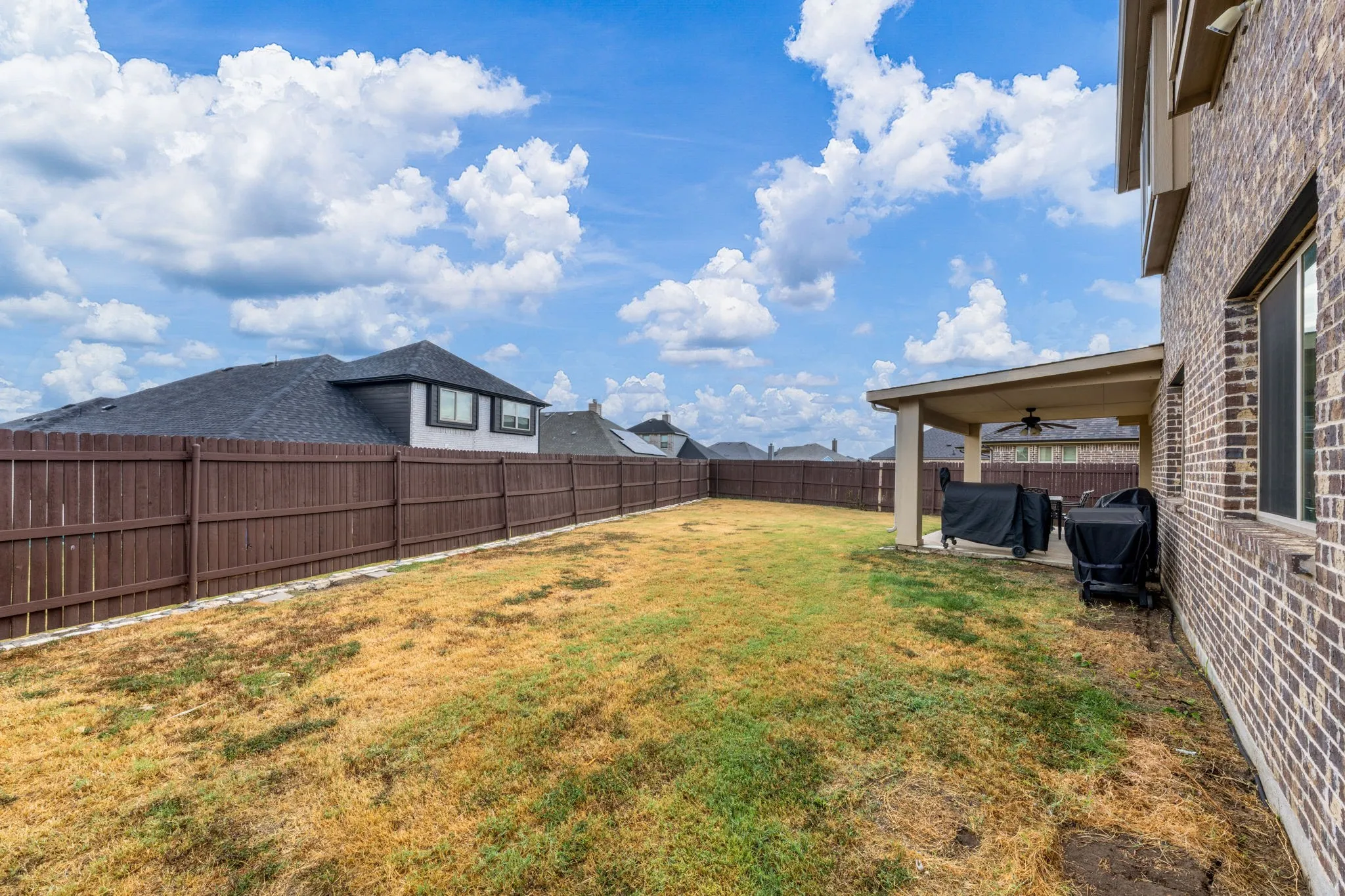 Expansive backyard featuring a covered patio with a ceiling fan, brick exterior, and a privacy fence