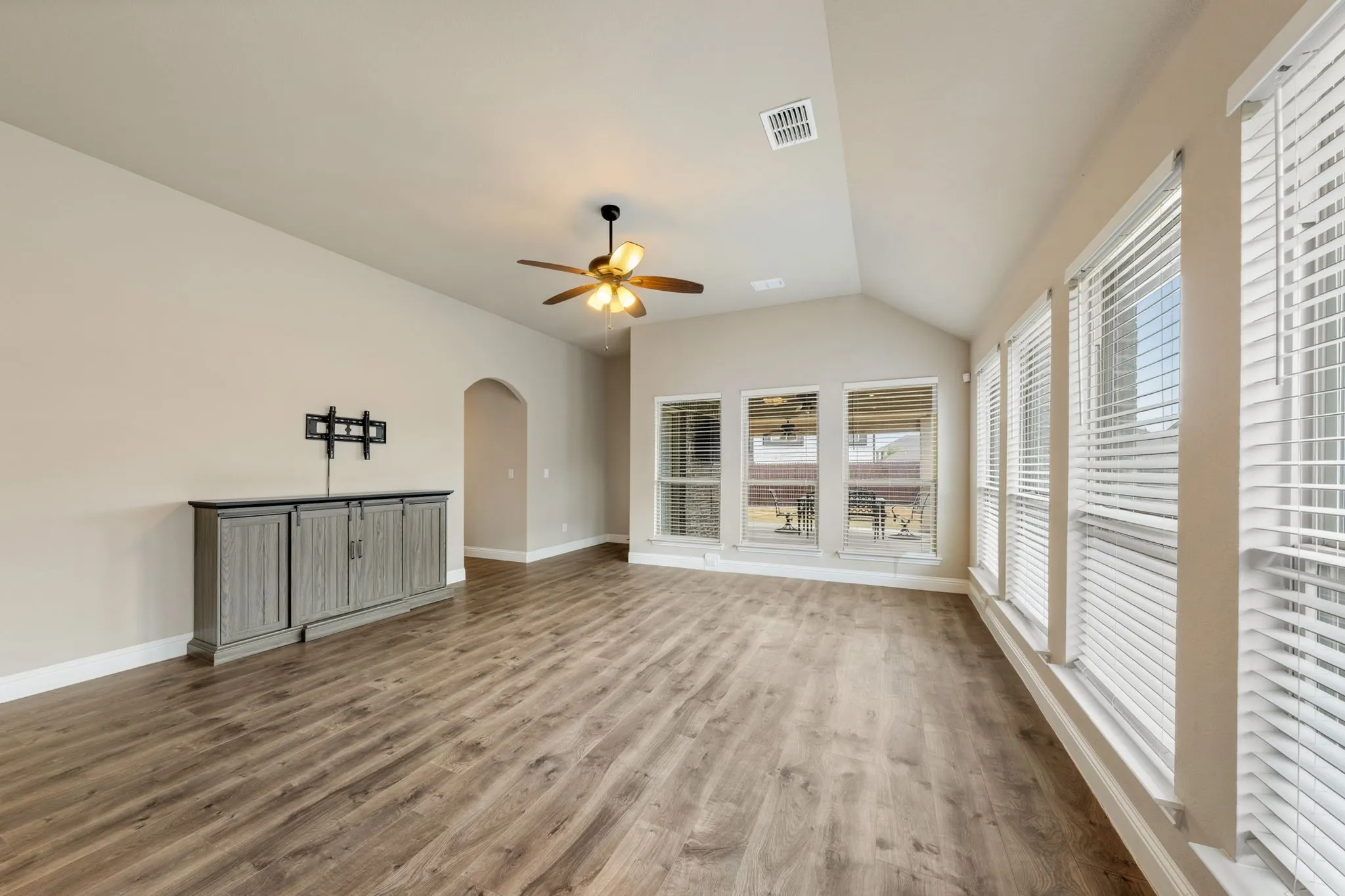 Vaulted ceiling with a ceiling fan, wood-finish flooring, arched doorway, and multiple windows with blinds