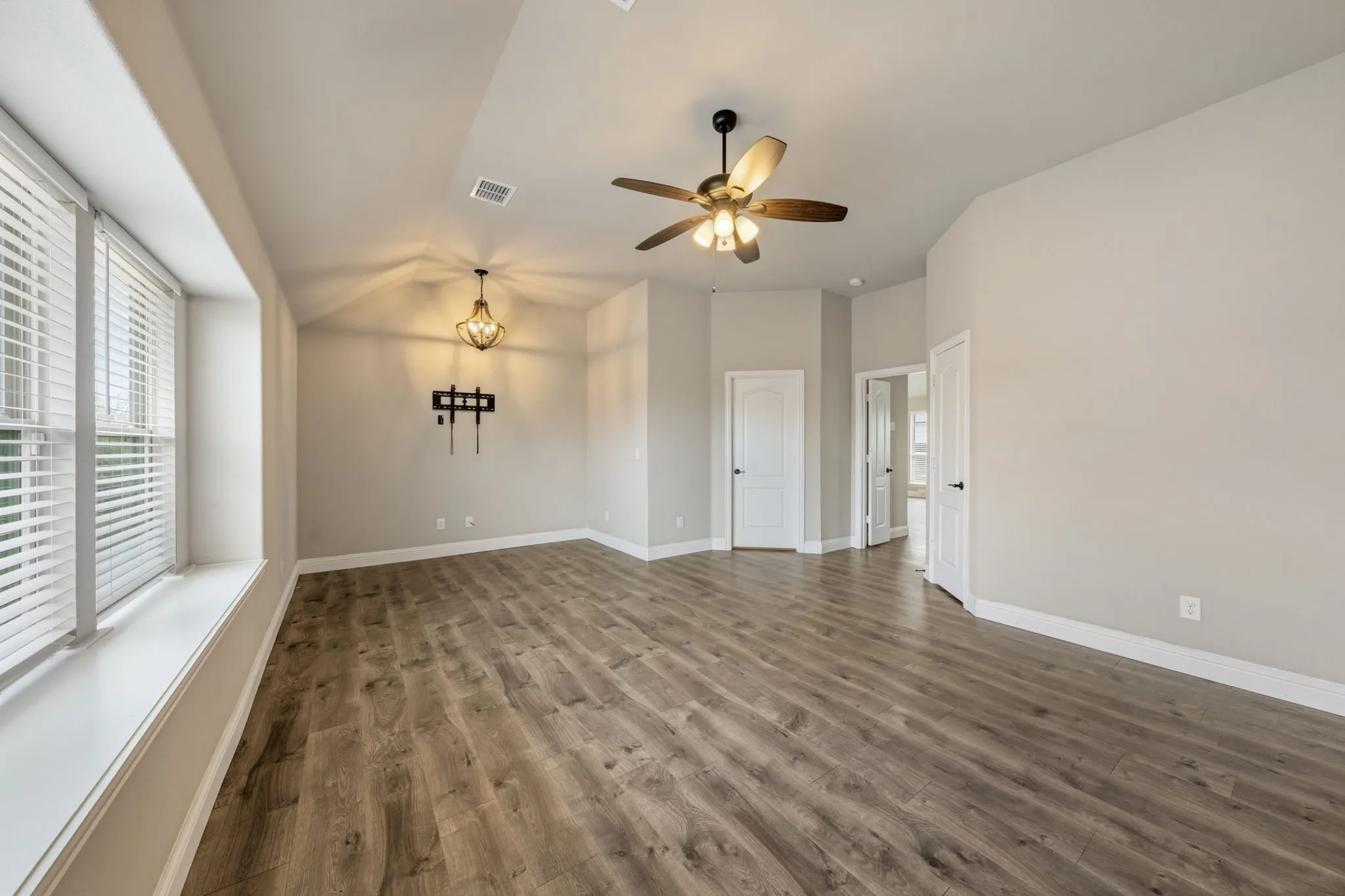 Spacious room featuring wood-finish flooring, a contemporary ceiling fan, and a decorative chandelier