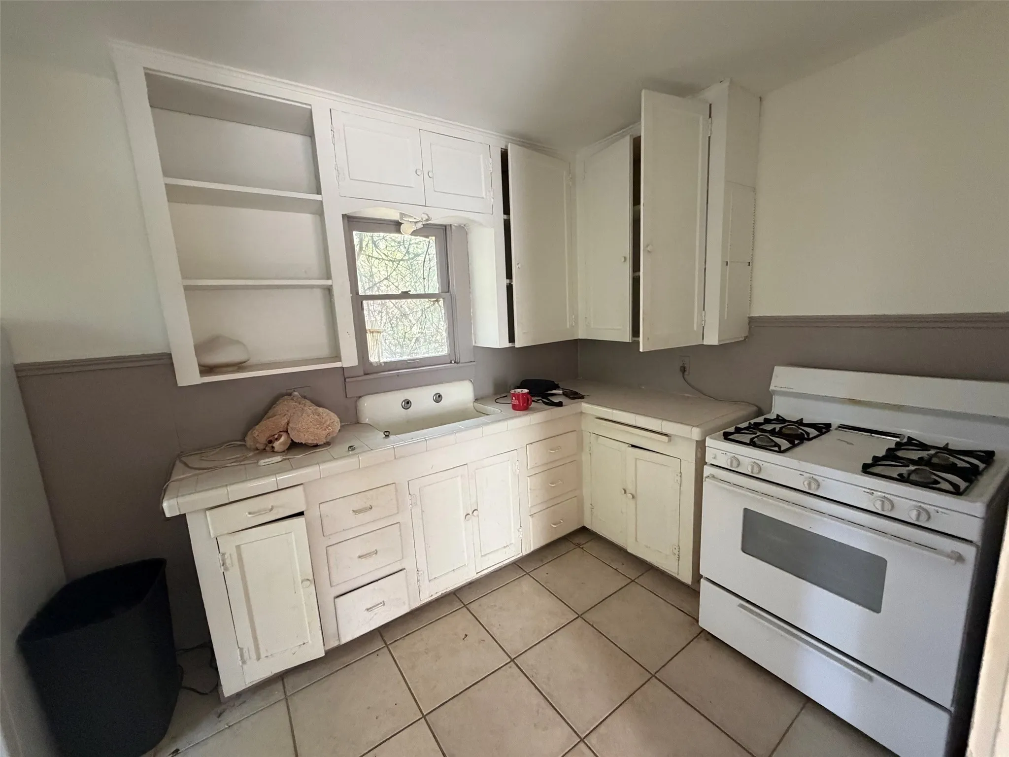 Kitchen featuring white cabinetry, tile countertops, an integrated sink, a gas range, and tile flooring