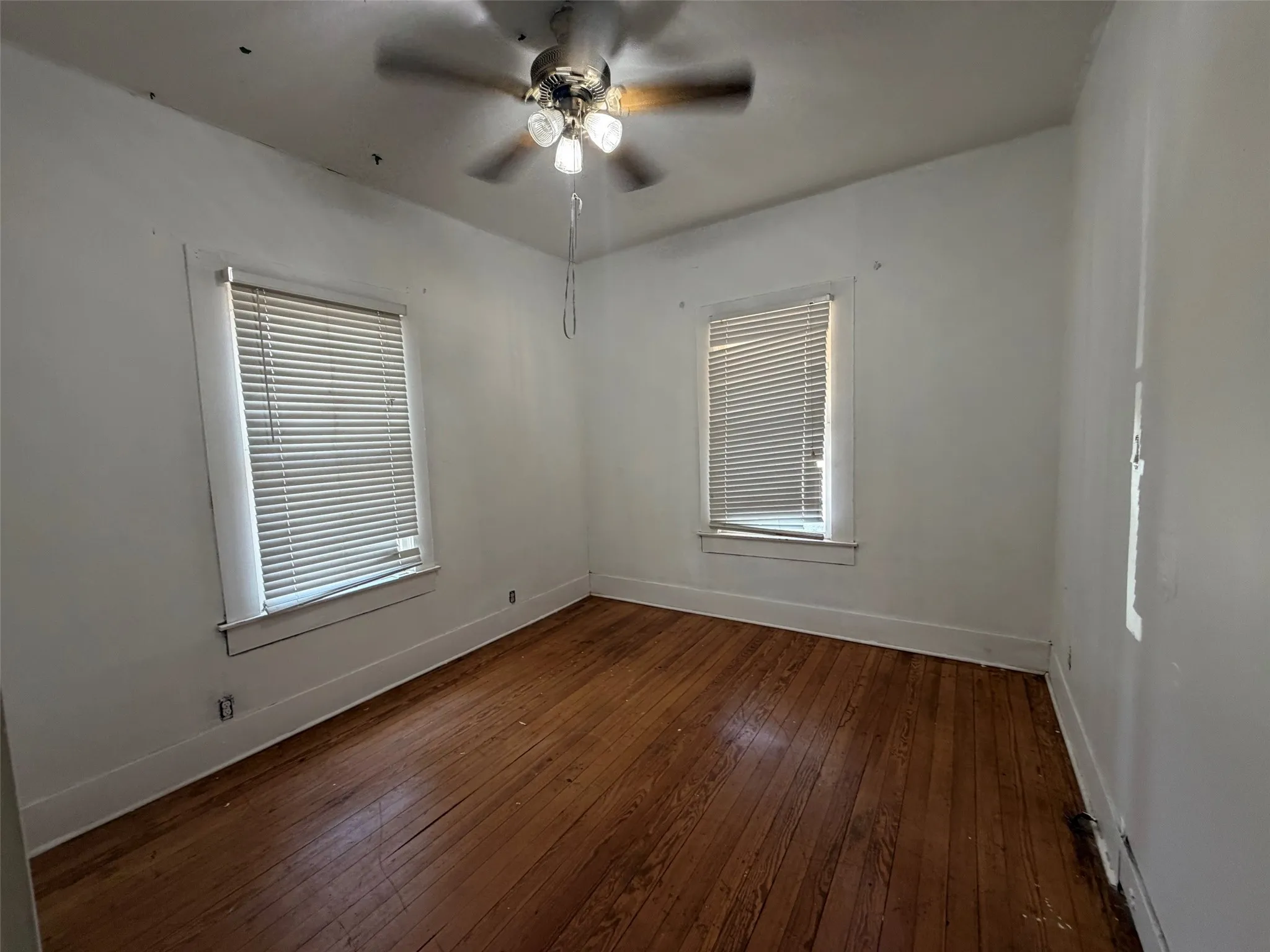 Wood-finish flooring with white trim, two windows, and a ceiling fan with integrated lighting