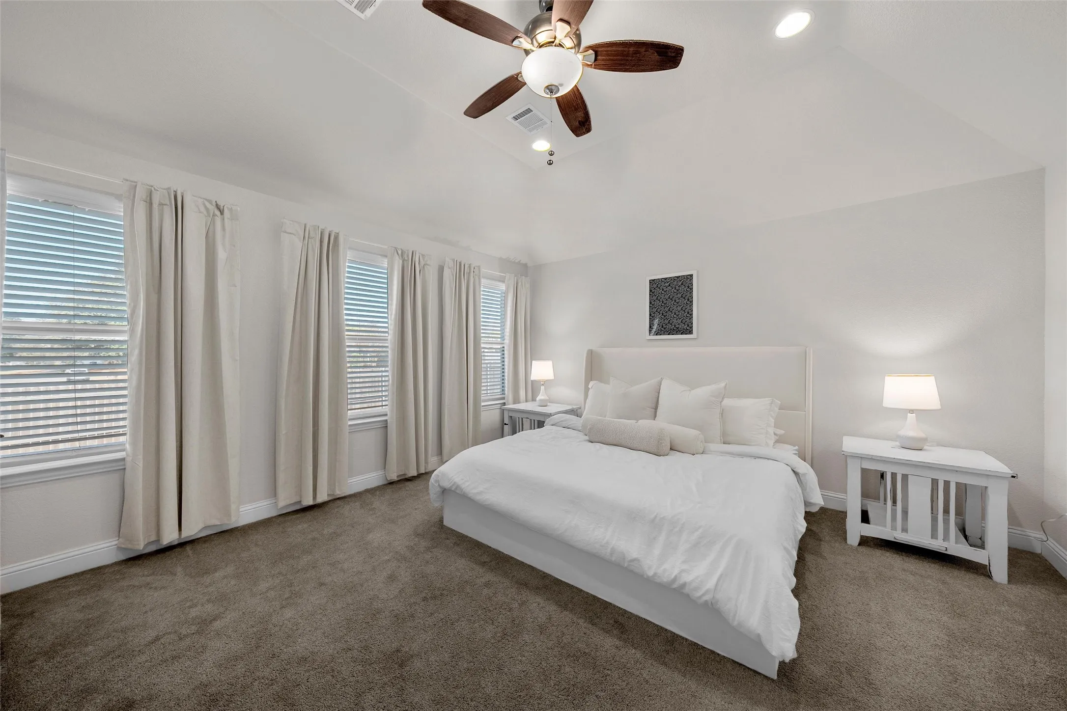 Vaulted ceiling, ceiling fan with integrated lighting, recessed lighting, multiple windows with blinds, and neutral tone carpet flooring