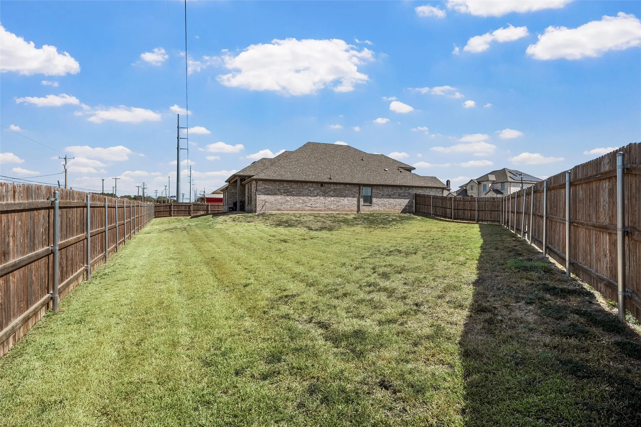 Expansive backyard with a manicured lawn, full privacy fencing, and a brick-clad exterior