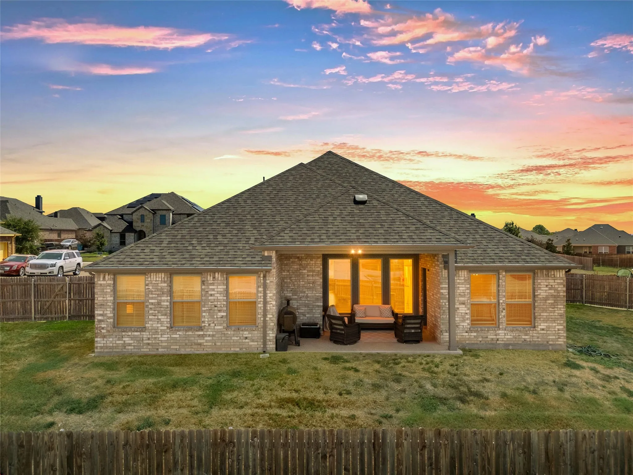 Rear brick exterior with a covered patio, multiple windows, and a sloped grassy yard