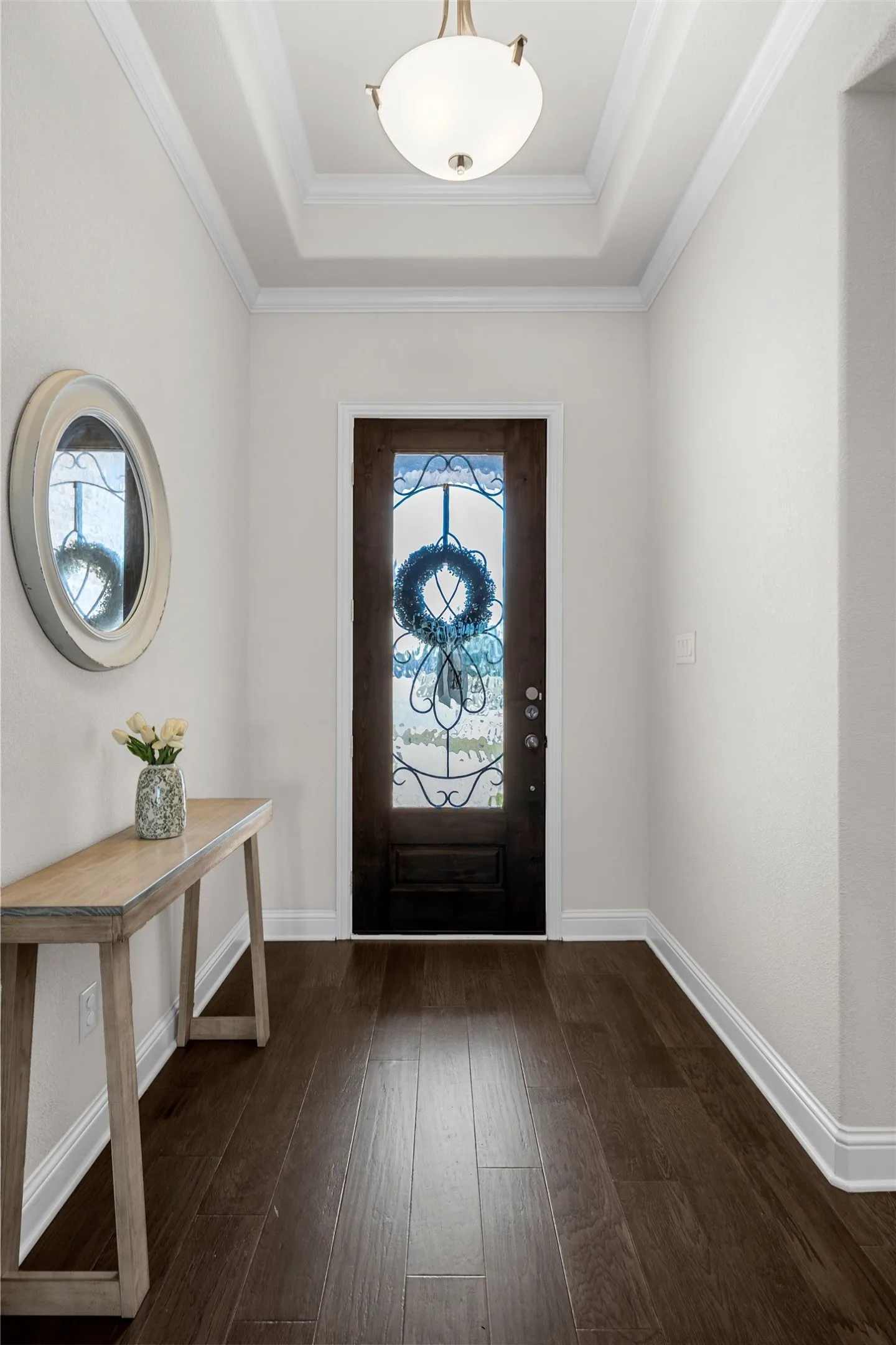 Tray ceiling with a decorative light fixture, wood-finish flooring, and a dark-stained entry door with decorative glass