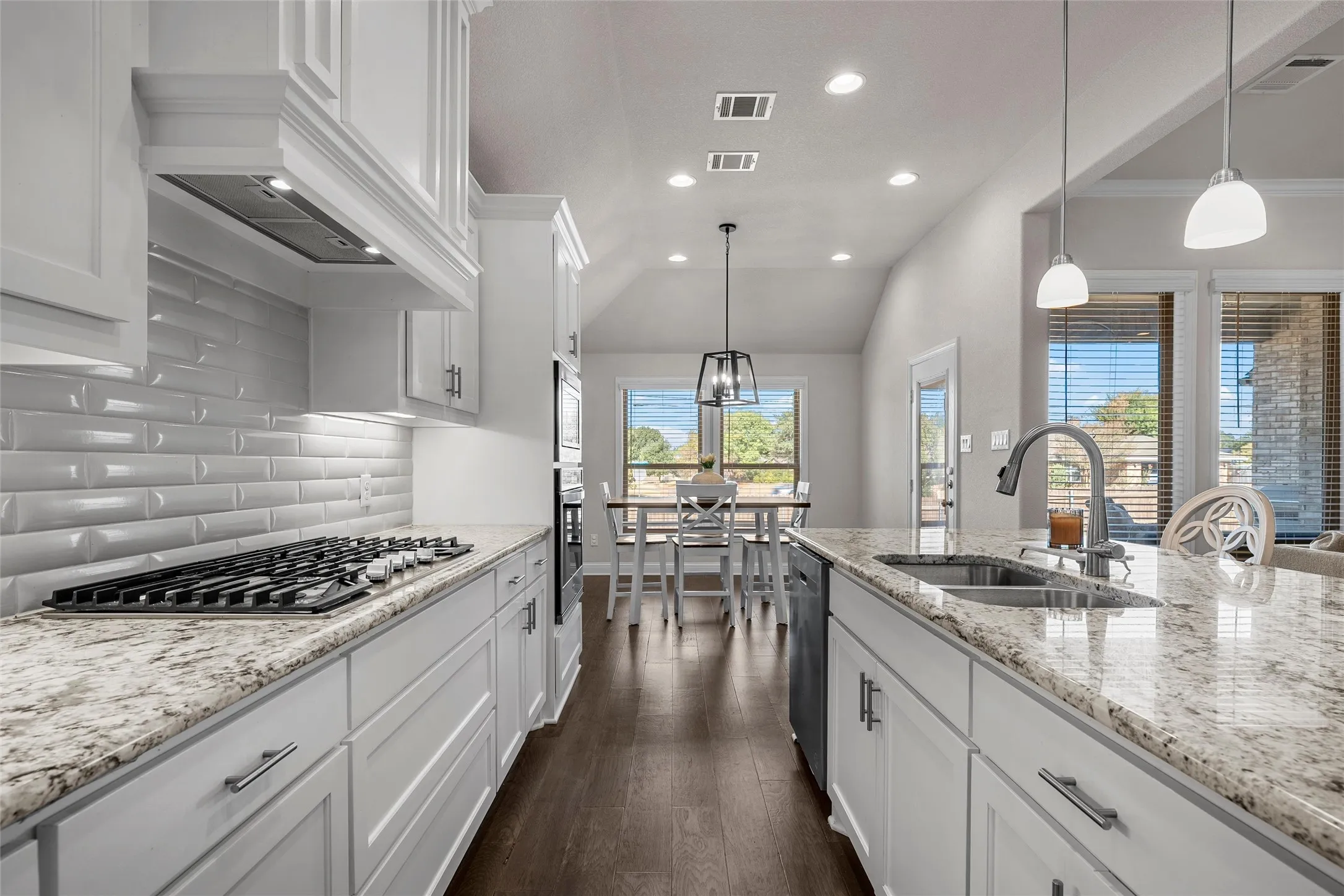 White shaker cabinetry, light-toned countertops, gas cooktop, built-in dishwasher, and wood-finish flooring