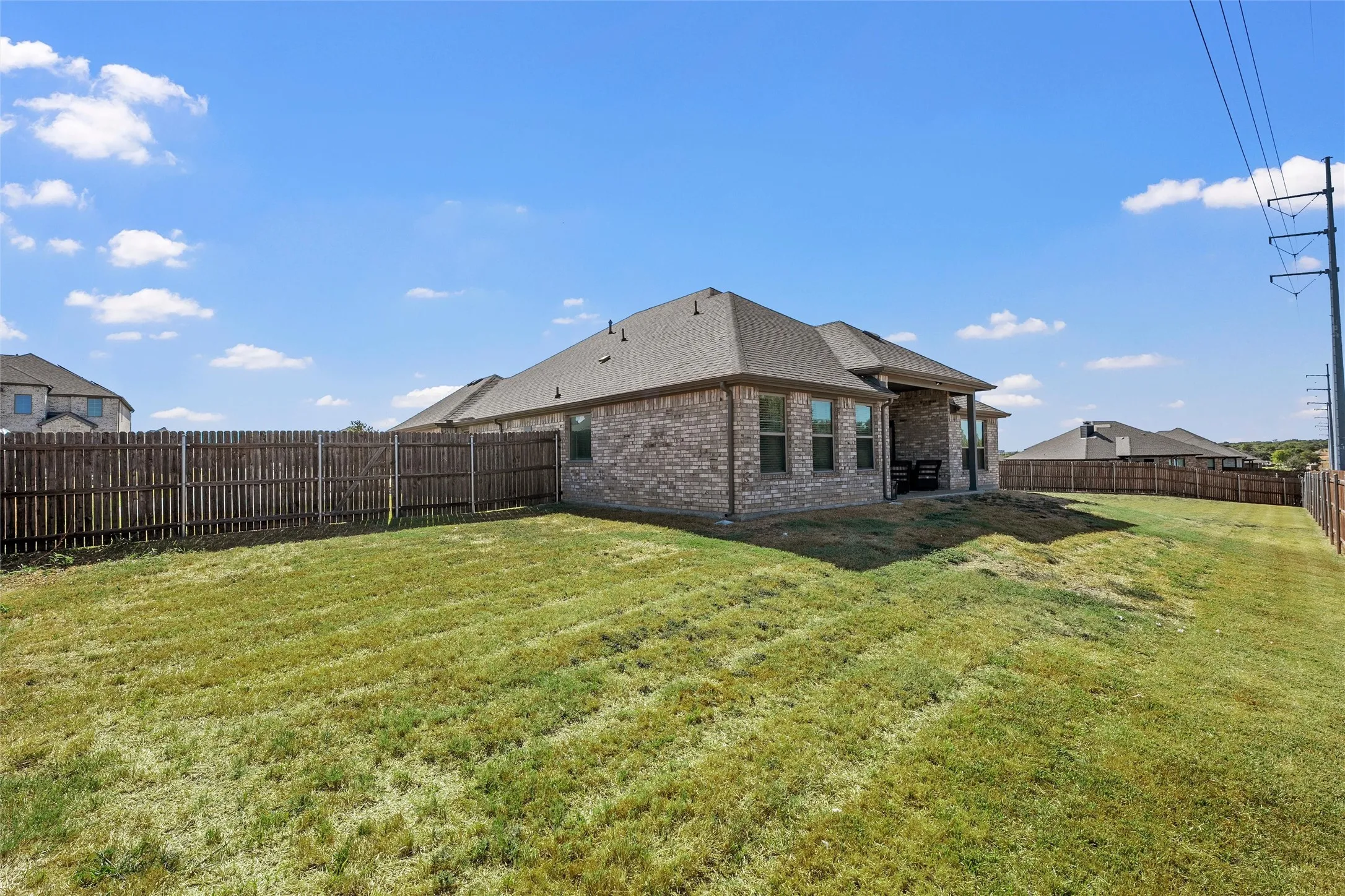 Expansive backyard featuring a privacy fence, a brick exterior, multiple windows, and a covered patio