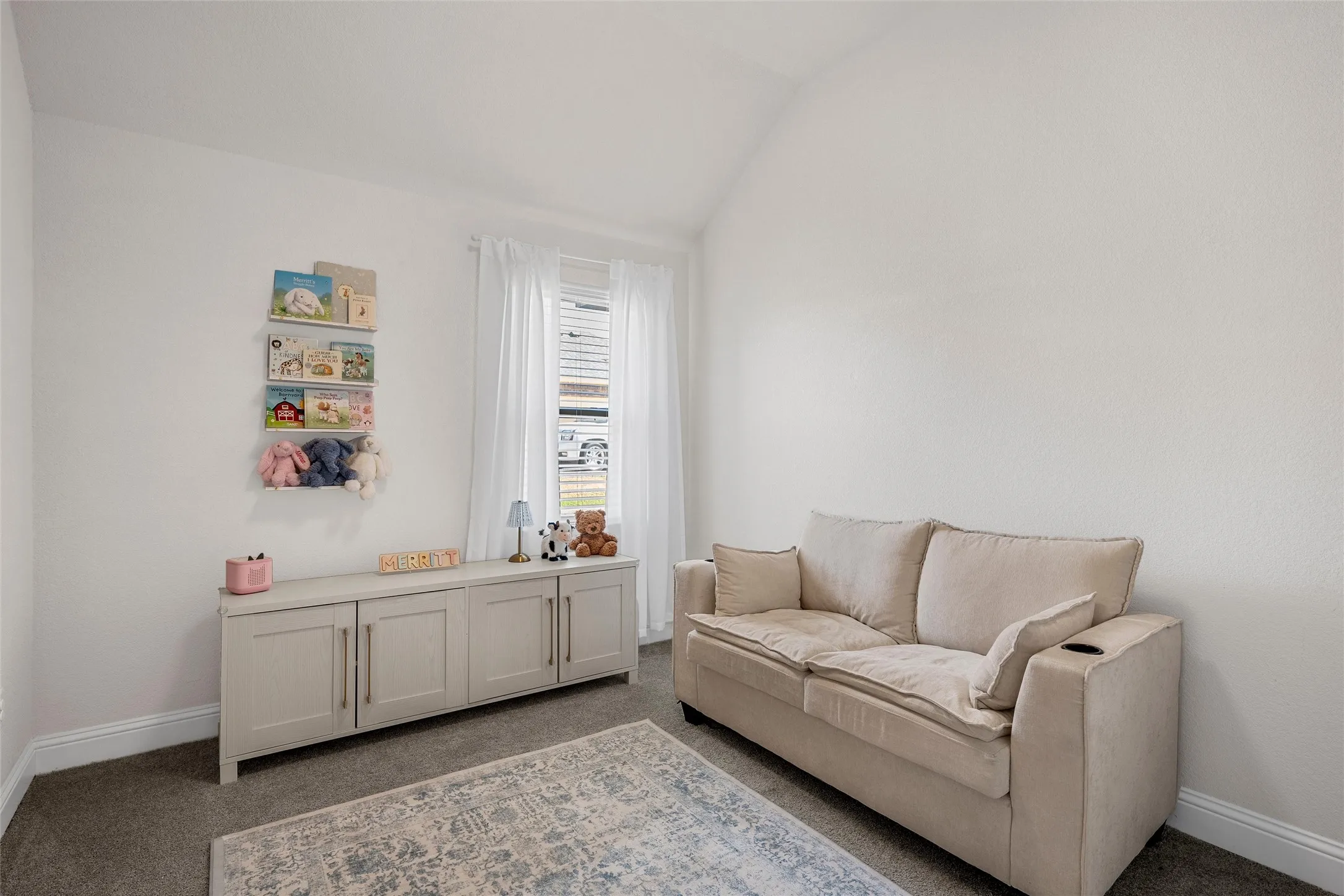 Vaulted ceiling, window with white blinds, neutral wall paint, built-in cabinetry with hardware, and carpet flooring
