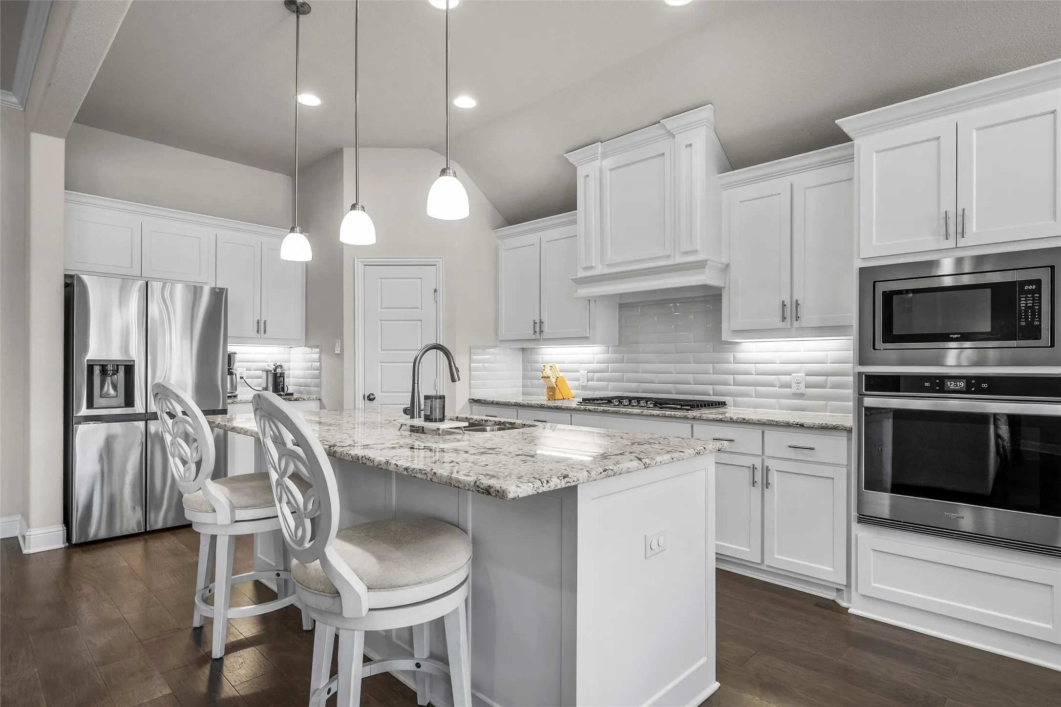 Kitchen featuring an island with stone countertops, white cabinetry, stainless steel appliances, a subway tile backsplash, and wood-finish flooring
