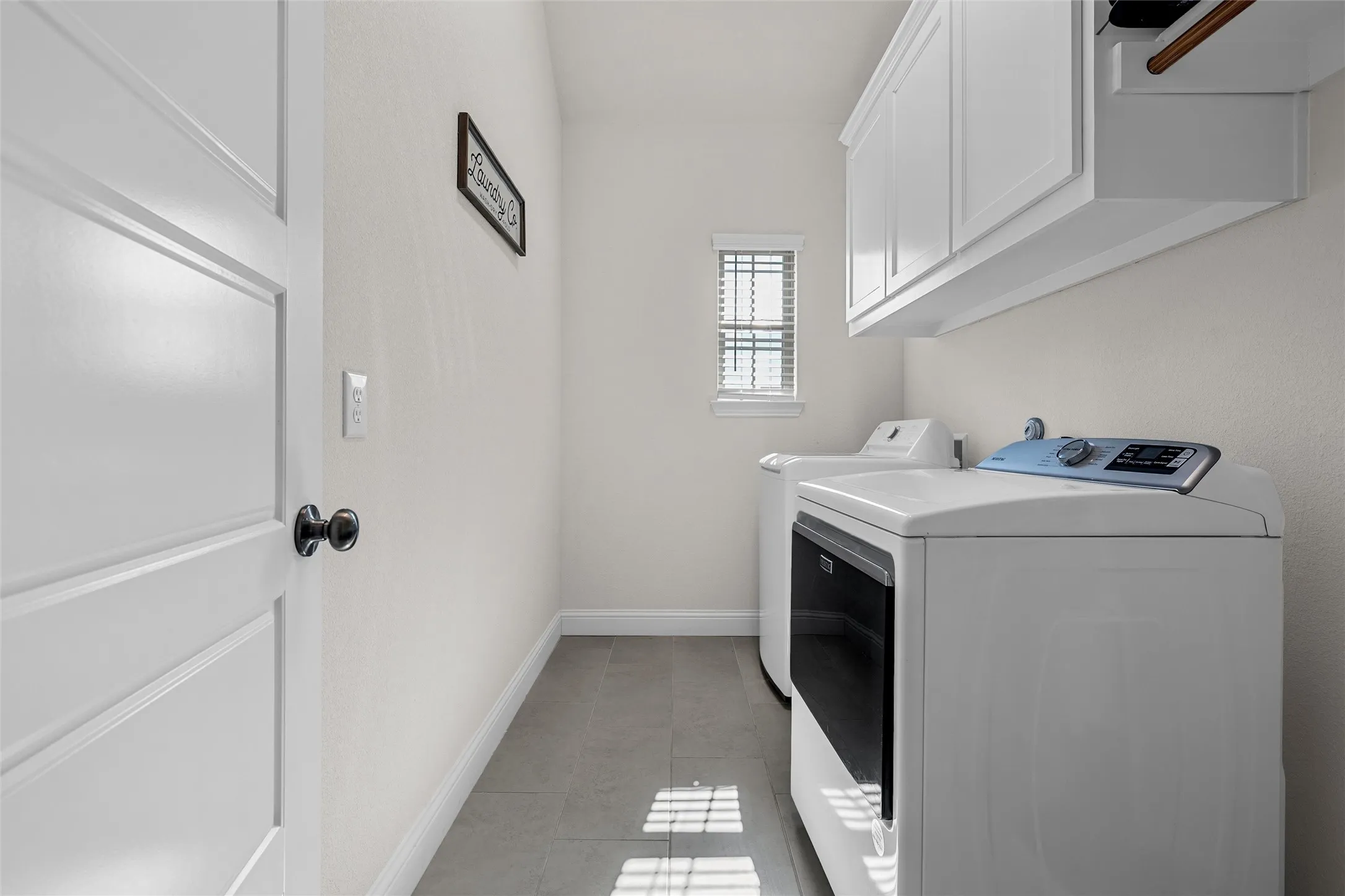 Laundry area with built-in cabinetry, grey tile flooring, and a window with blinds
