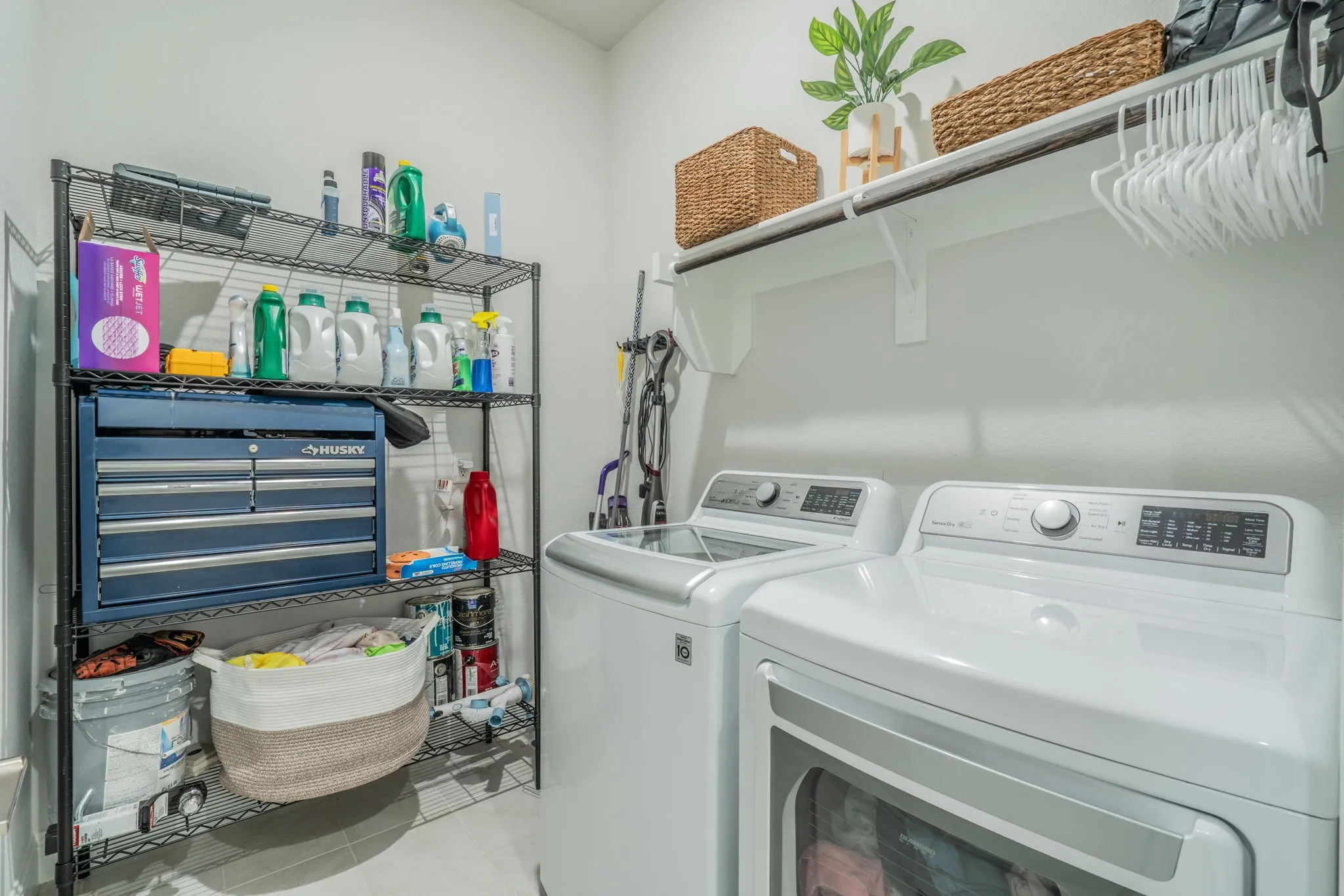 Laundry area featuring tile flooring, a wall-mounted shelf with a hanging rod, and wire shelving