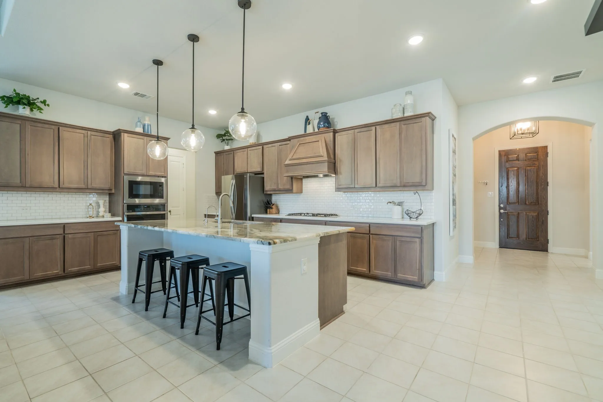 Spacious kitchen featuring an expansive center island, integrated stainless steel appliances, wood-finish cabinetry, and a subway tile backsplash