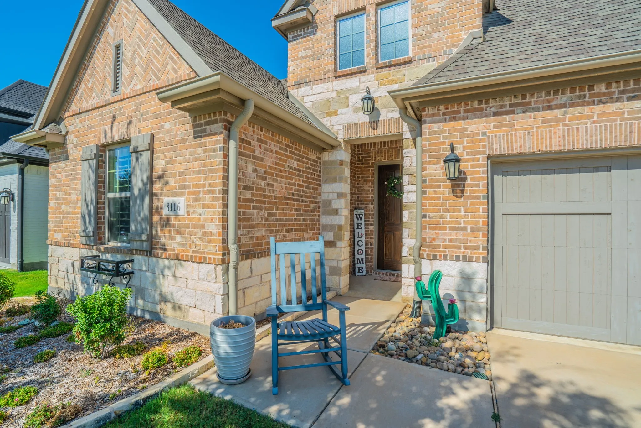 Brick and stone facade, covered entry, attached garage, exterior lighting fixtures, and decorative window shutters