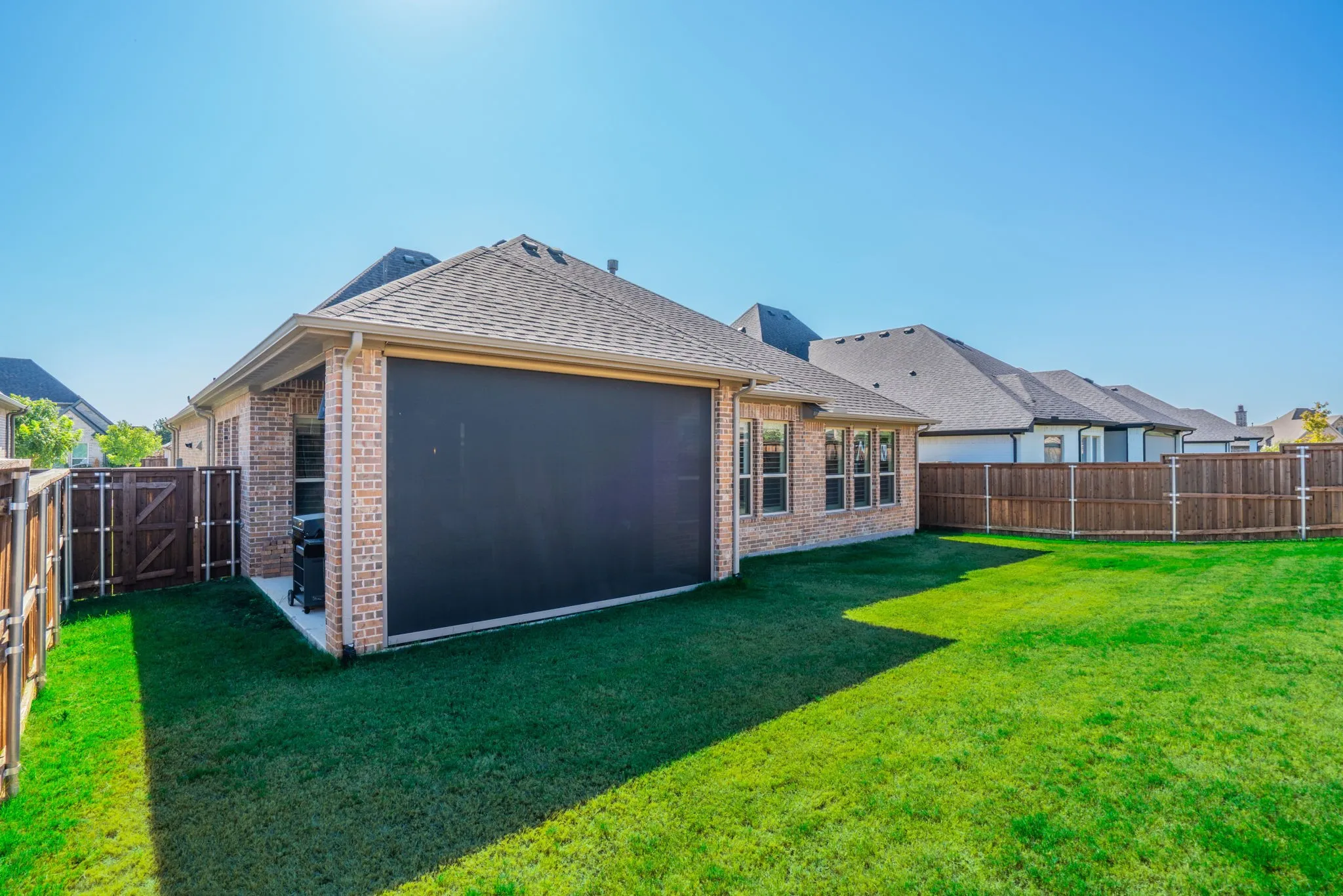 Expansive green lawn with a covered patio featuring a retractable screen, brick exterior, and a privacy fence