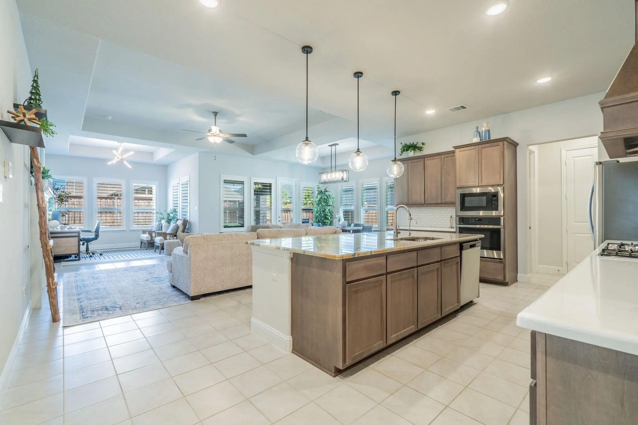 Open-concept kitchen with light-toned cabinetry, a spacious island with a stone countertop, stainless steel appliances, and tile flooring