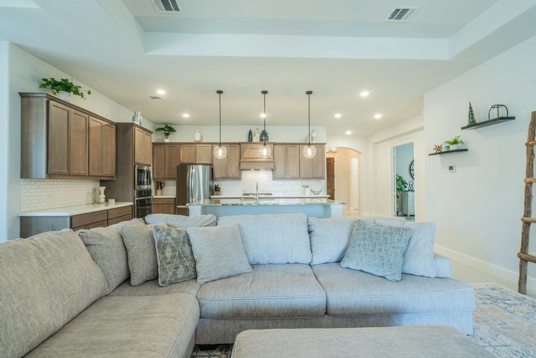 Recessed lighting, wood-finish cabinetry, stainless steel appliances, tiled backsplash, and an island with pendant lighting
