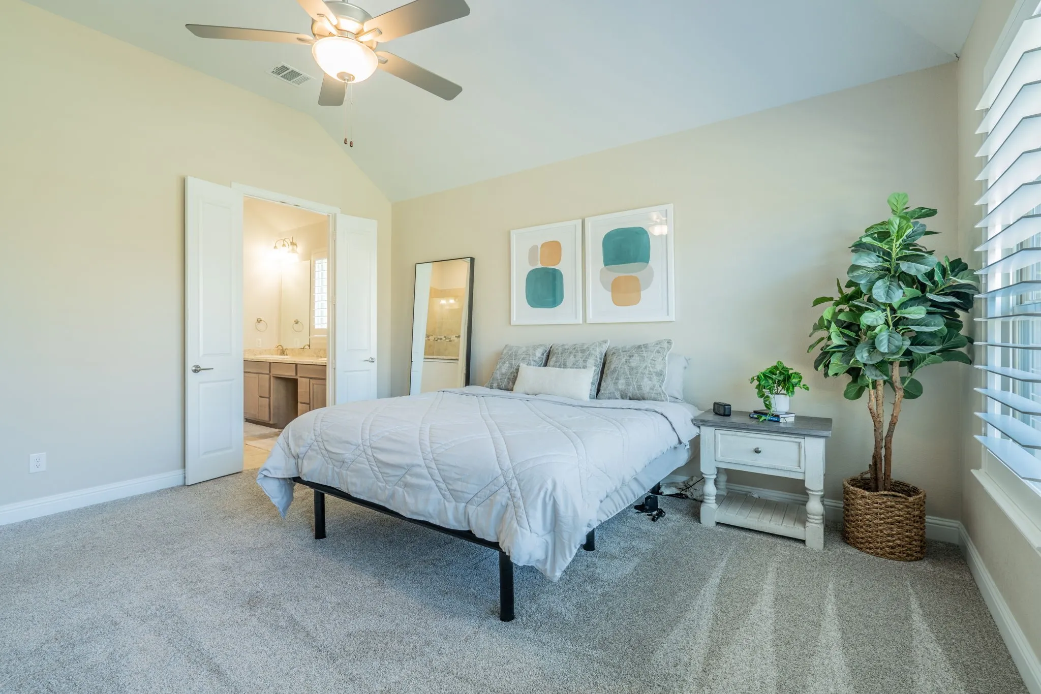 Vaulted ceiling with a ceiling fan, carpeted flooring, double-door entry to the bathroom, and window with horizontal blinds