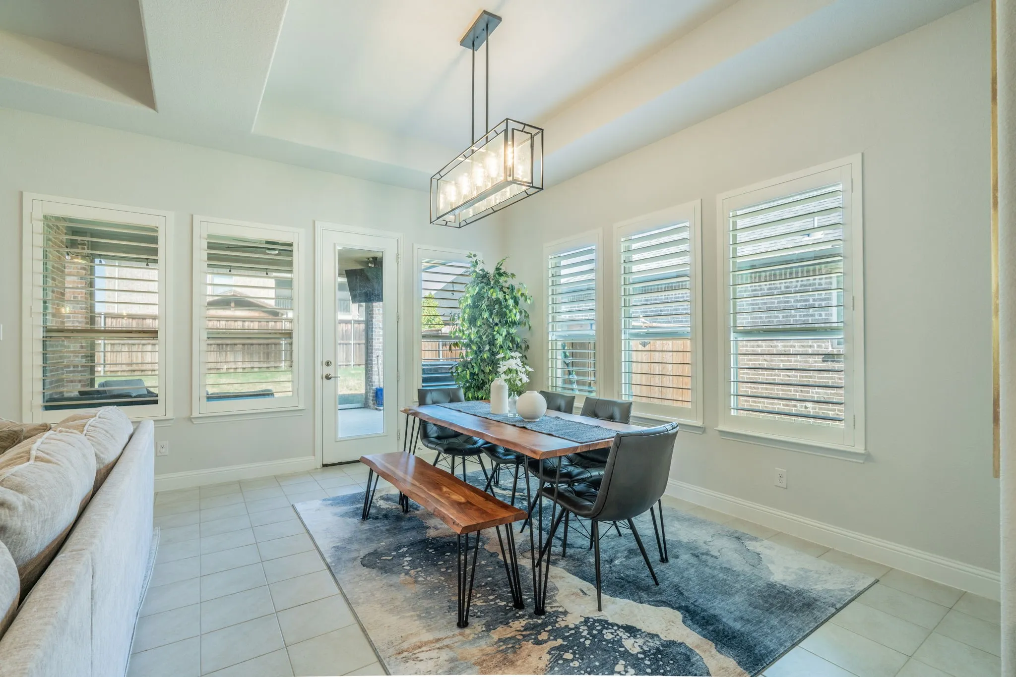 Recessed tray ceiling, multiple windows with white plantation shutters, glass-paneled exterior door, and light-toned tile flooring