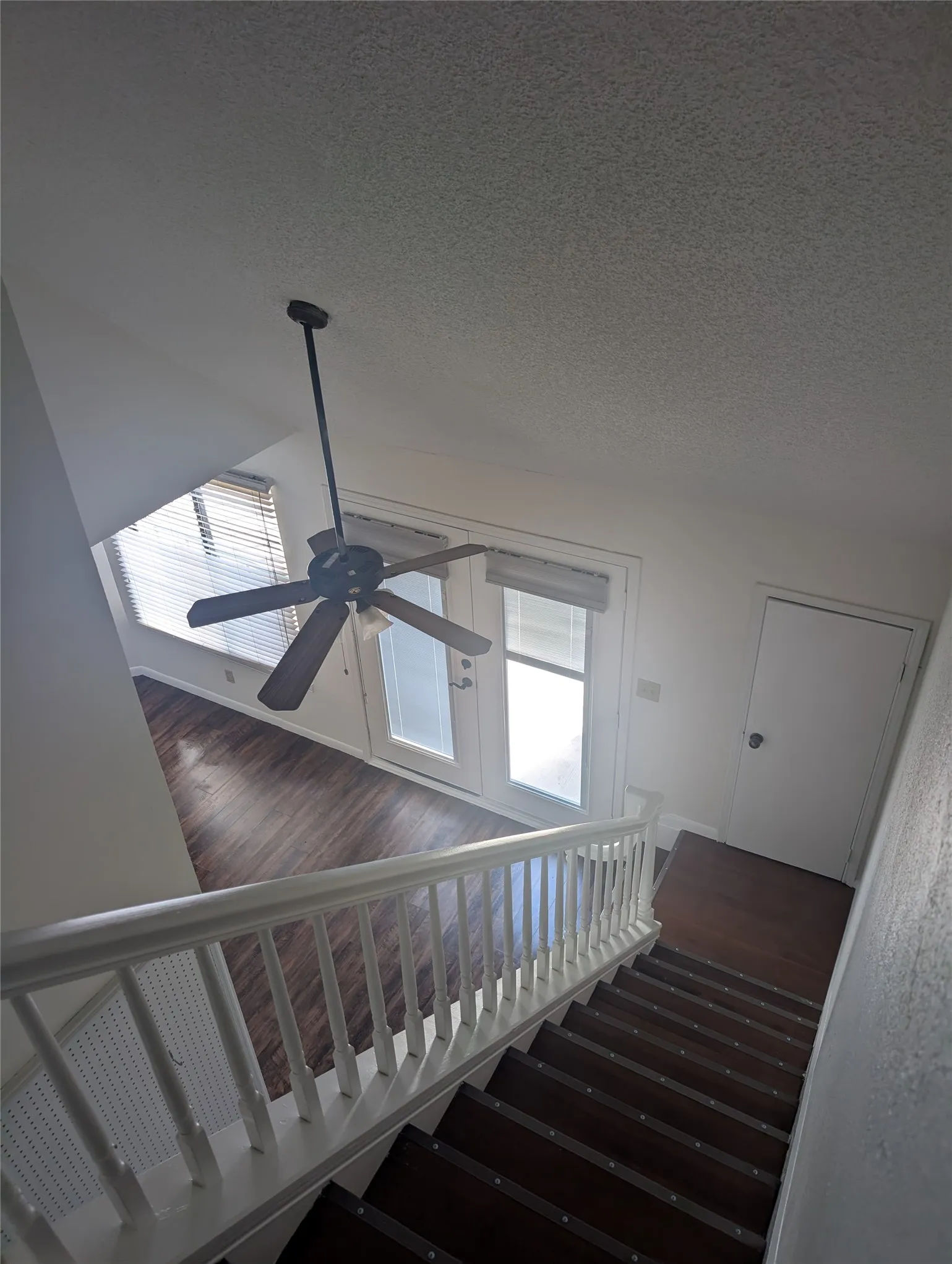 Wood-finish flooring, white painted railing, ceiling fan, and double panel door with blinds