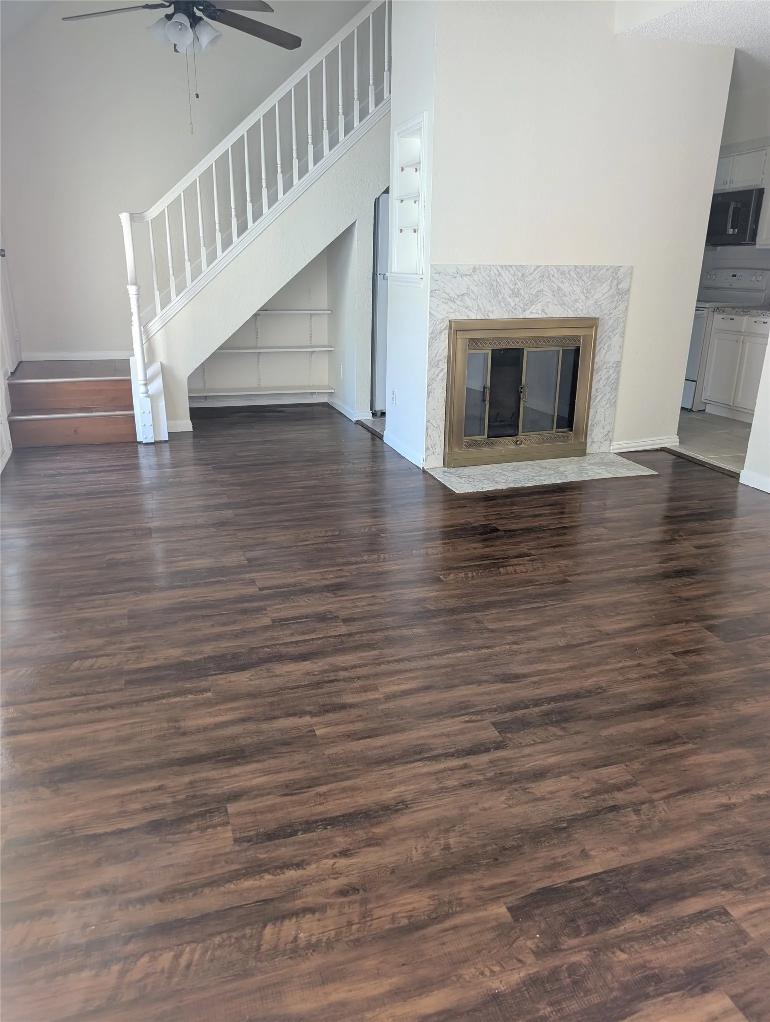 Wood-finish flooring throughout, white baluster staircase, built-in shelving, marble-look fireplace surround, and a ceiling fan