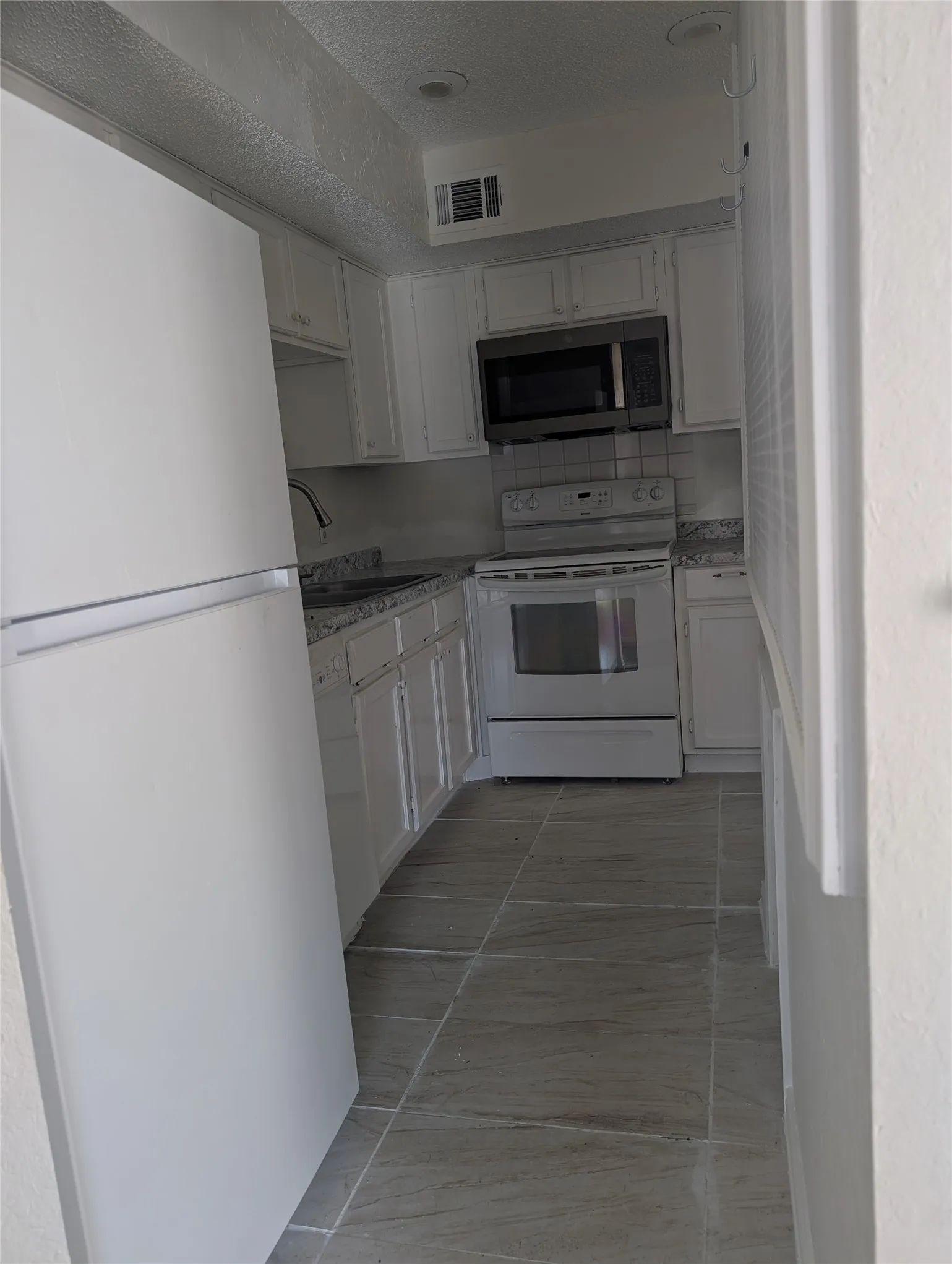 Kitchen featuring white cabinetry, stone-finish countertops, stainless steel microwave, and tile flooring