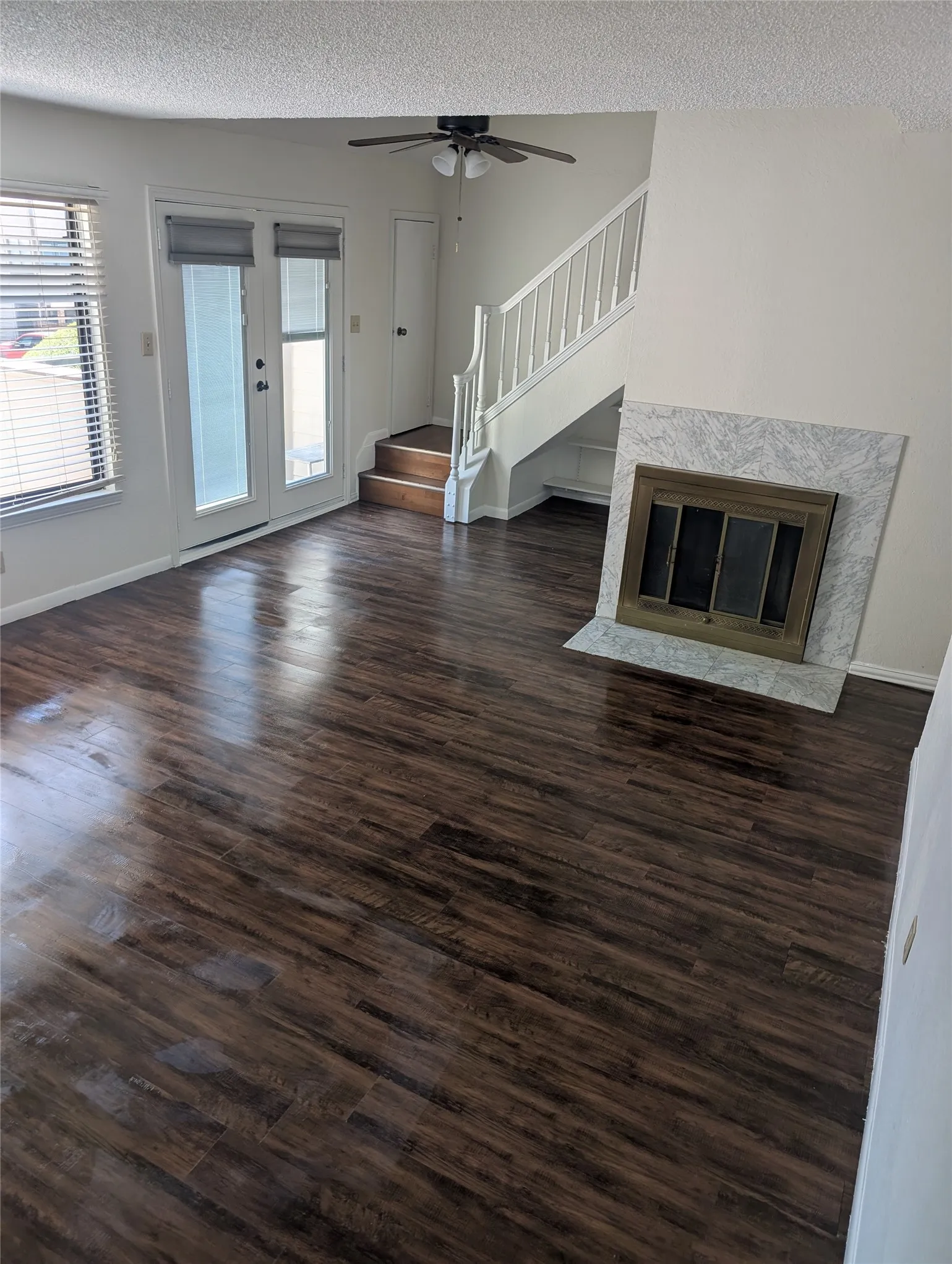 Spacious living area featuring wood-finish flooring, a fireplace with a stone surround, and a ceiling fan