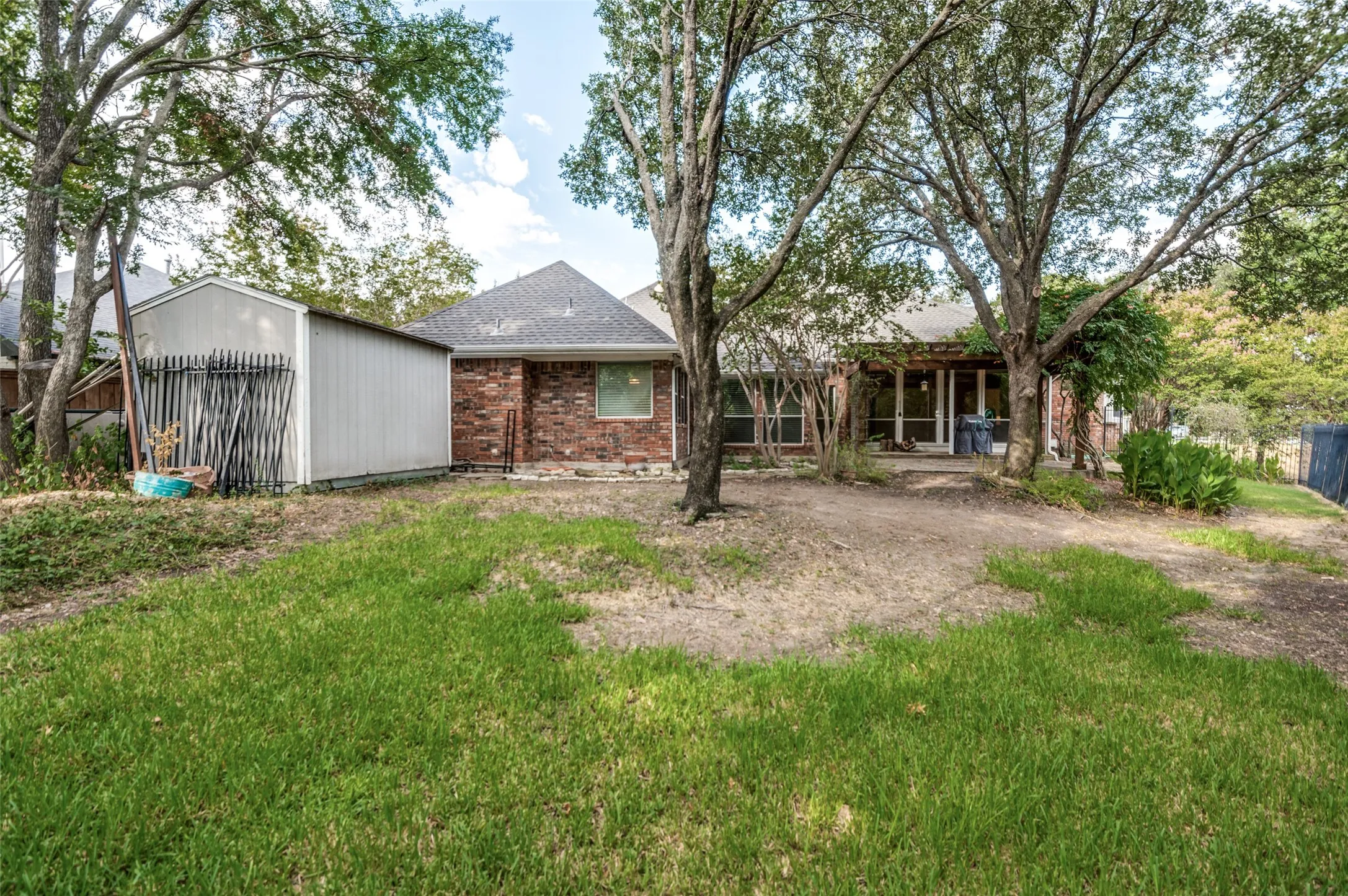 Brick exterior with a covered patio, mature trees, and a detached storage shed