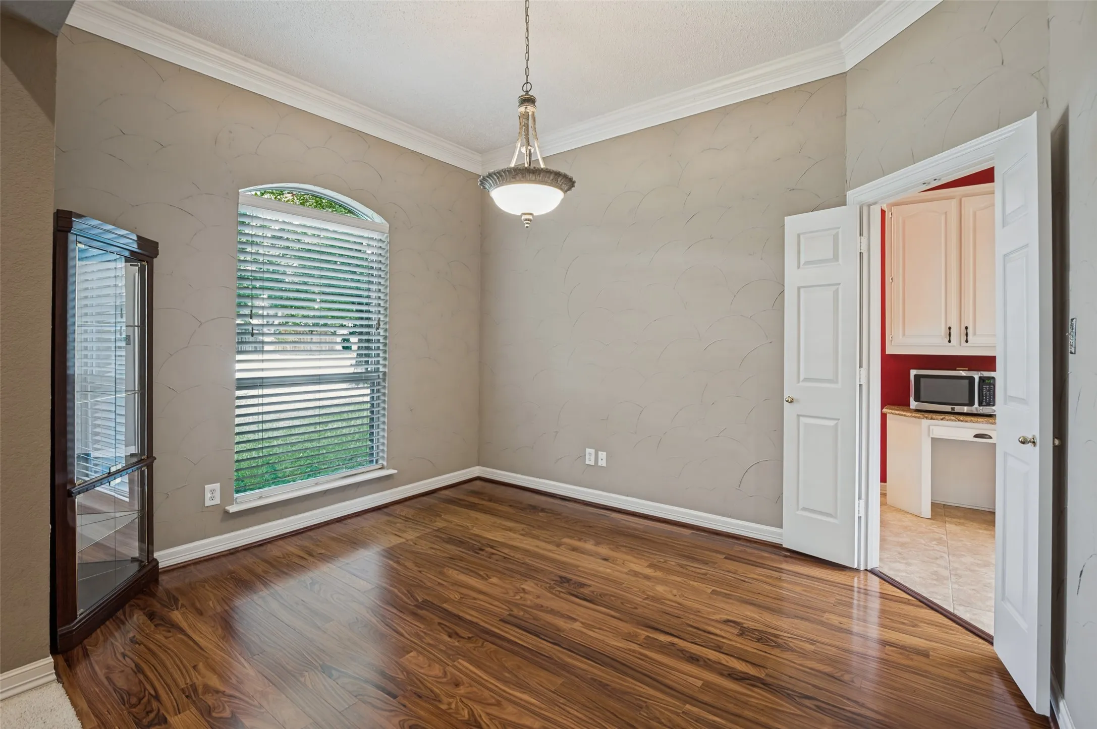 Arched window with blinds, wood-finish flooring, crown molding, and a built-in display cabinet