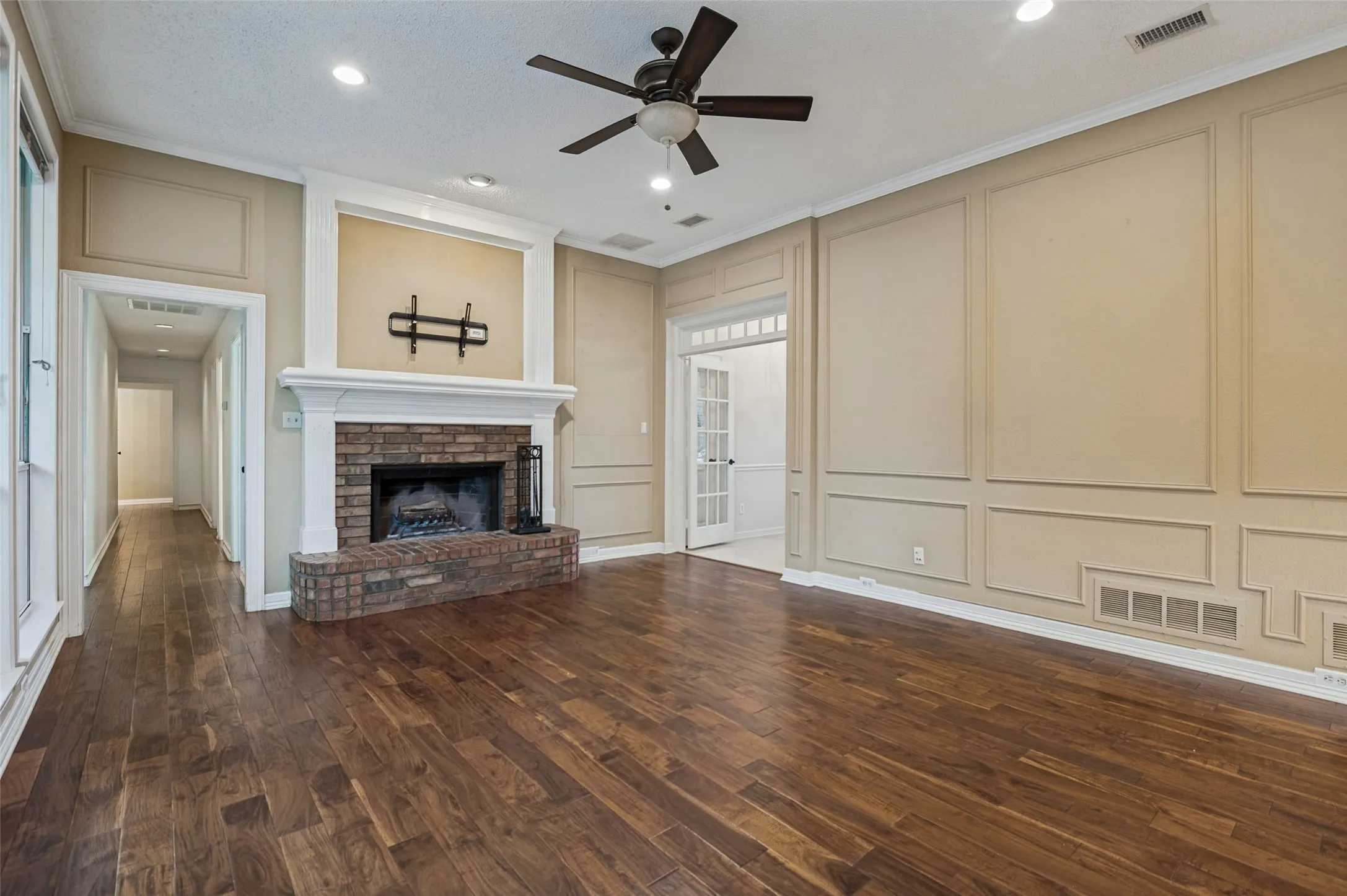 Wood-finish flooring, brick fireplace with a substantial mantel, recessed lighting, ceiling fan, and decorative wall molding