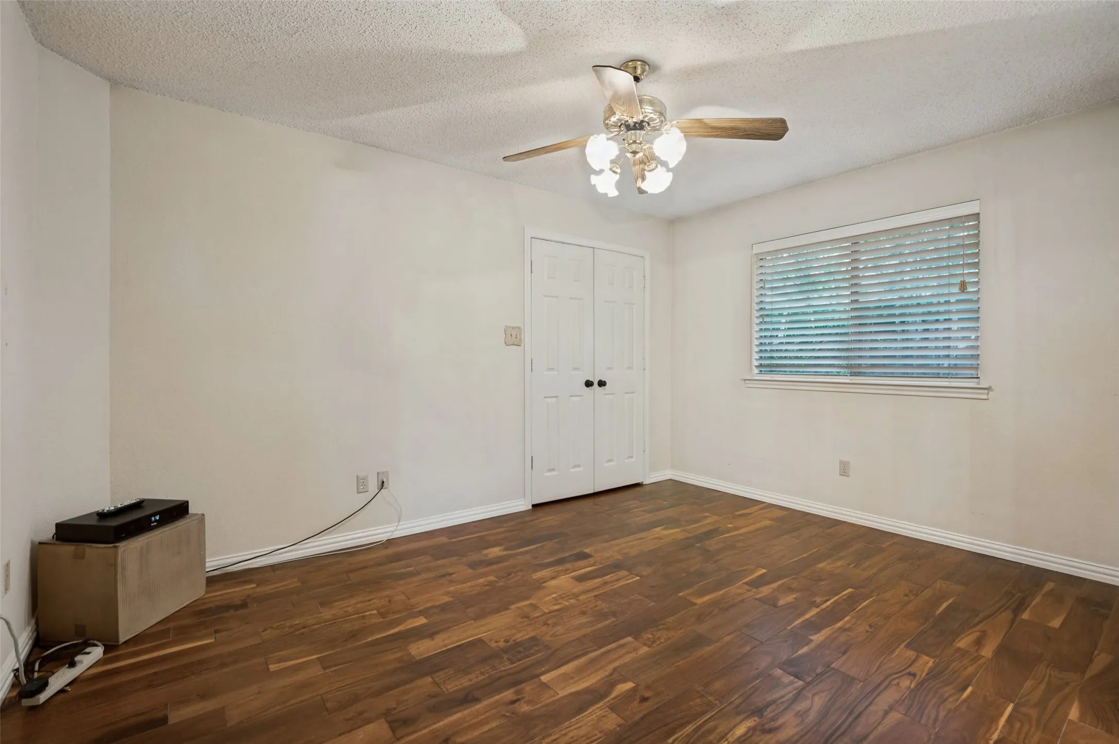 Wood-finish flooring, white double bi-fold closet doors, ceiling fan with light fixture, and a window with blinds