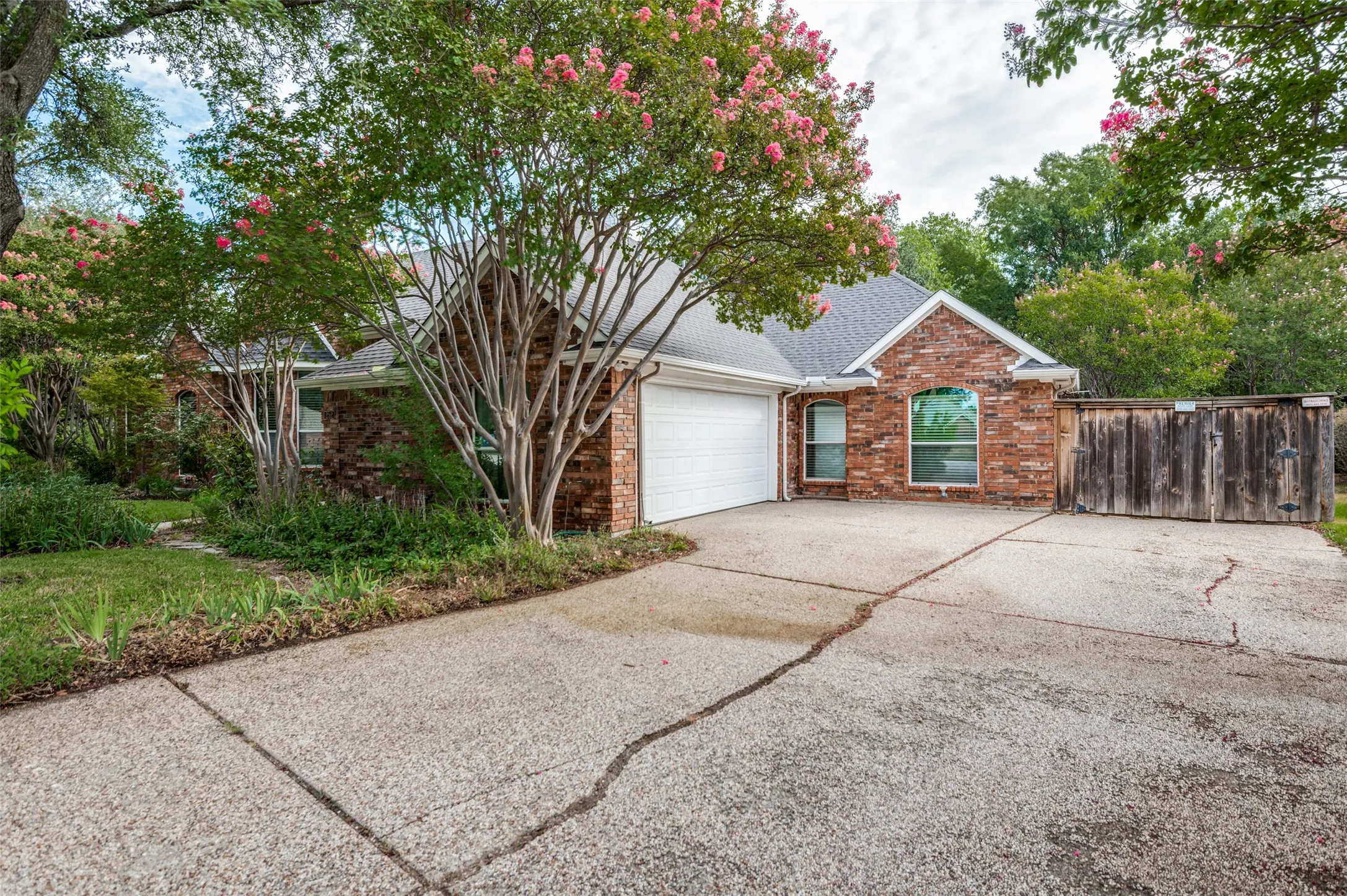 Brick exterior with a gabled roofline, mature trees, and an attached garage with a white door