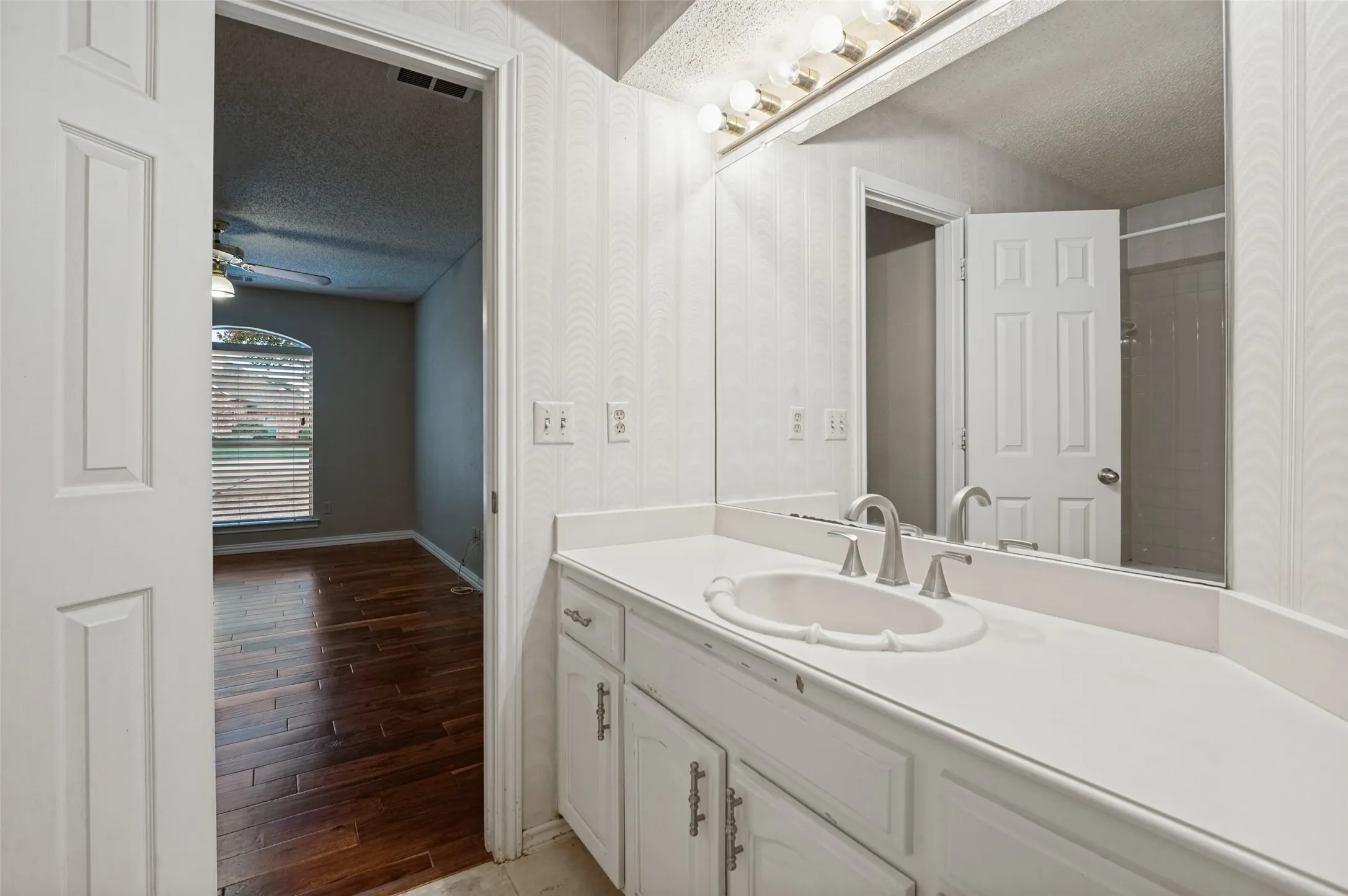 Vanity with integrated sink, brushed nickel faucet, large mirror, and overhead strip lighting