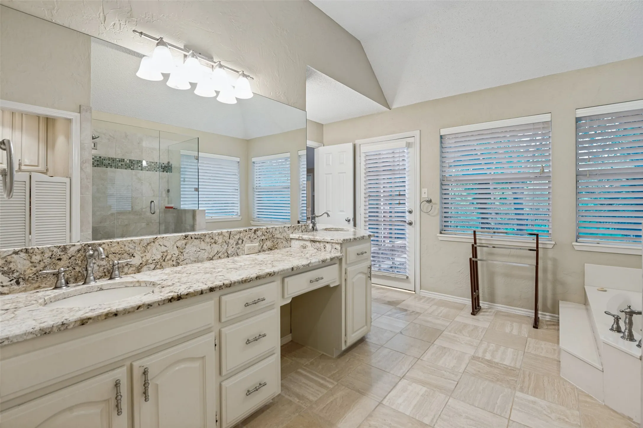 Dual vanity with granite countertop, large mirror, walk-in shower with glass enclosure, white soaking tub, and tiled flooring