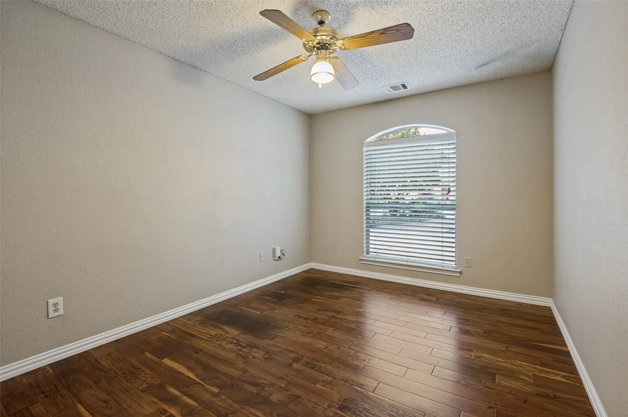 Arched window with blinds, wood-finish flooring, ceiling fan with integrated lighting, and neutral wall tones