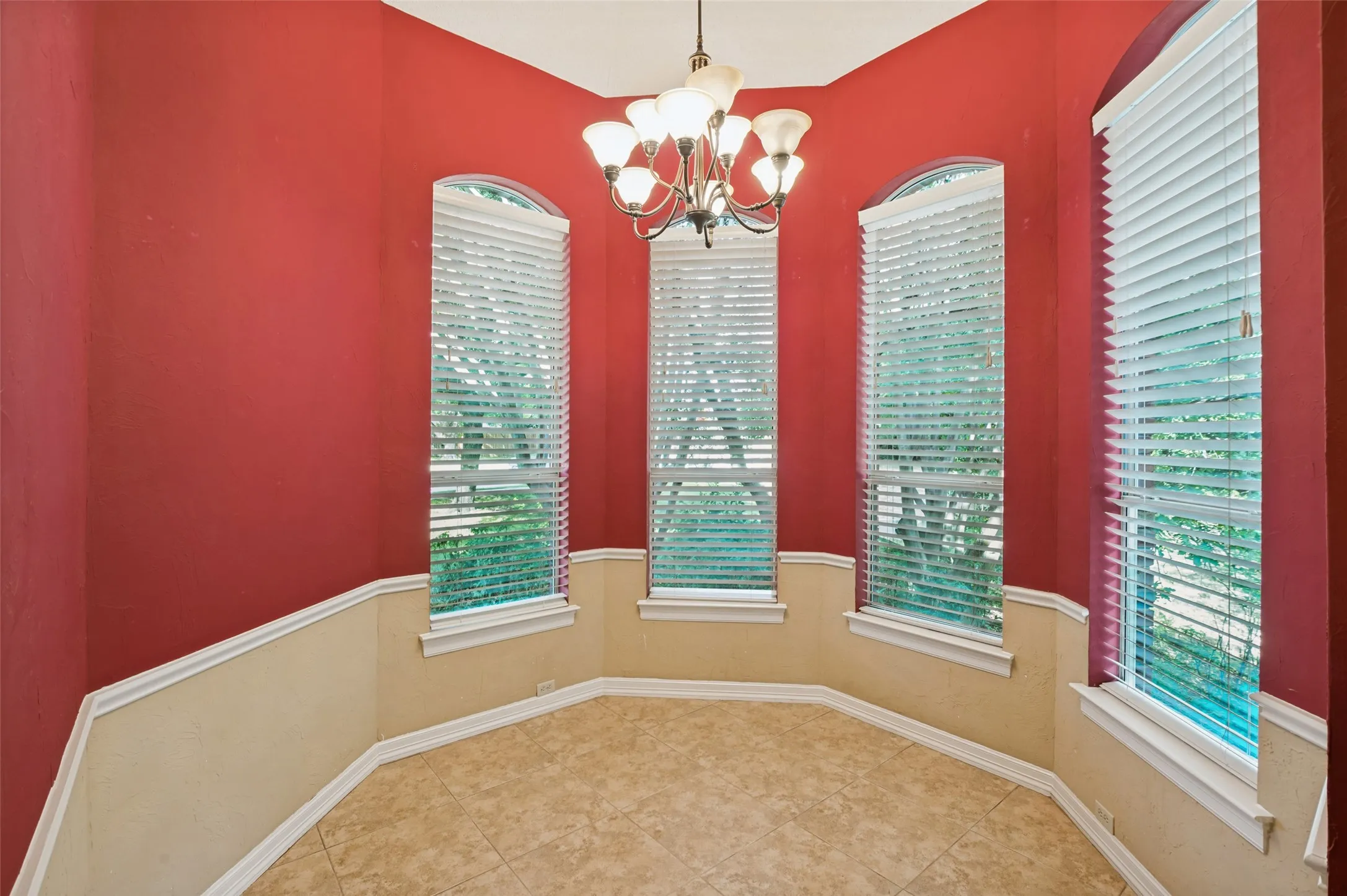 Bay window alcove featuring arched windows with blinds, a chandelier, and tile flooring