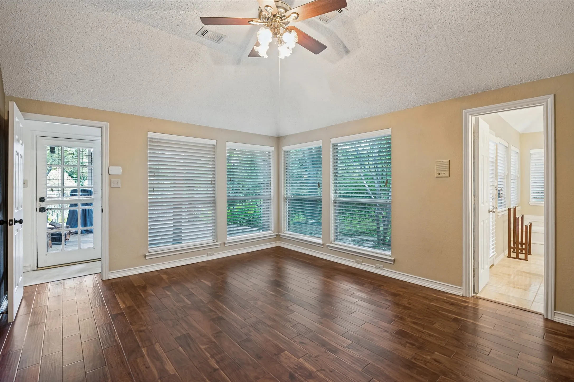Vaulted ceiling with a ceiling fan, wood-finish flooring, multiple windows with blinds, and a glass-paneled exterior door