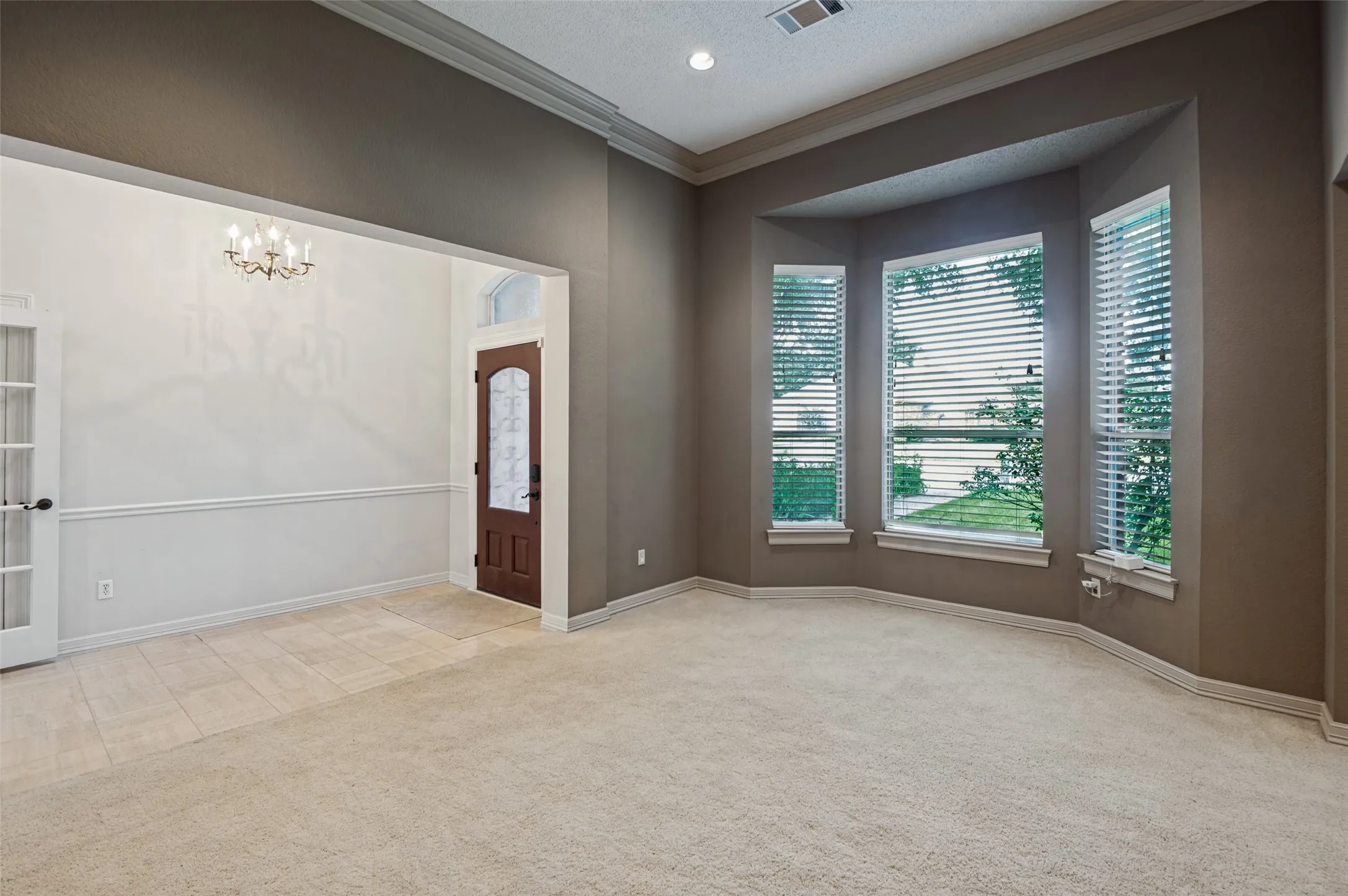 Bay window with multiple windows and blinds, crown molding, a chandelier, and a front entry door with a glass insert