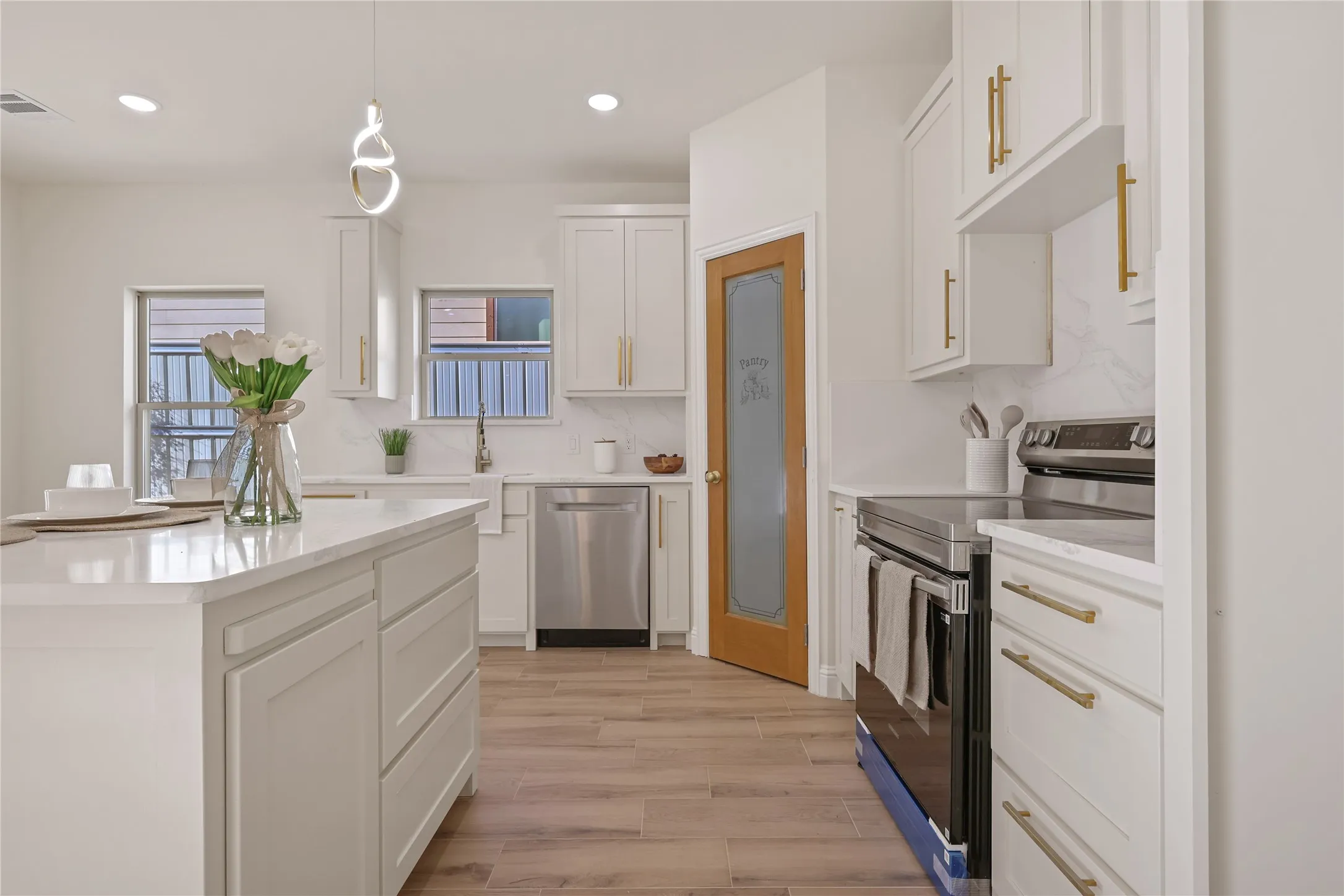 Kitchen featuring a central island, white shaker-style cabinetry with gold-tone hardware, stainless steel appliances, and wood-finish flooring