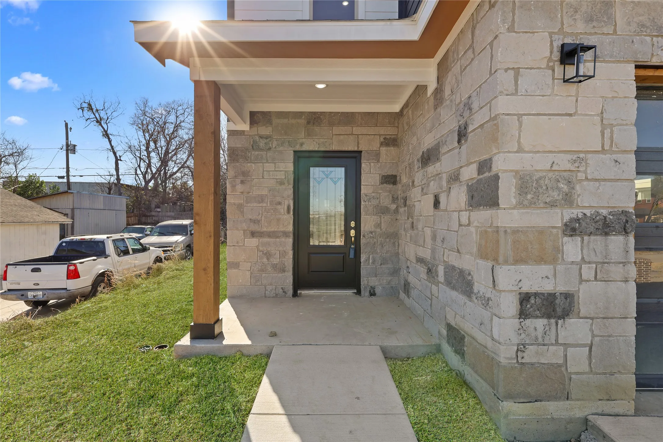 Stone veneer exterior with a covered porch featuring a wood column, recessed lighting, and a black front door with decorative glass