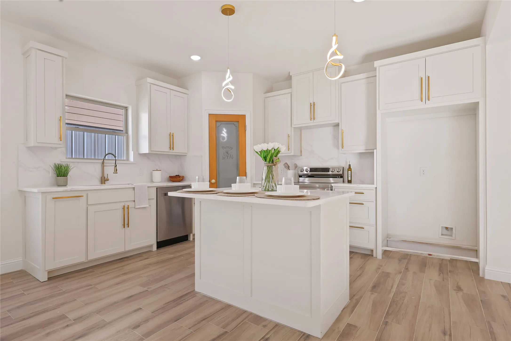 White cabinetry with gold-finish hardware, center island with solid surface countertop, stainless steel appliances, wood-finish flooring, and pendant lighting